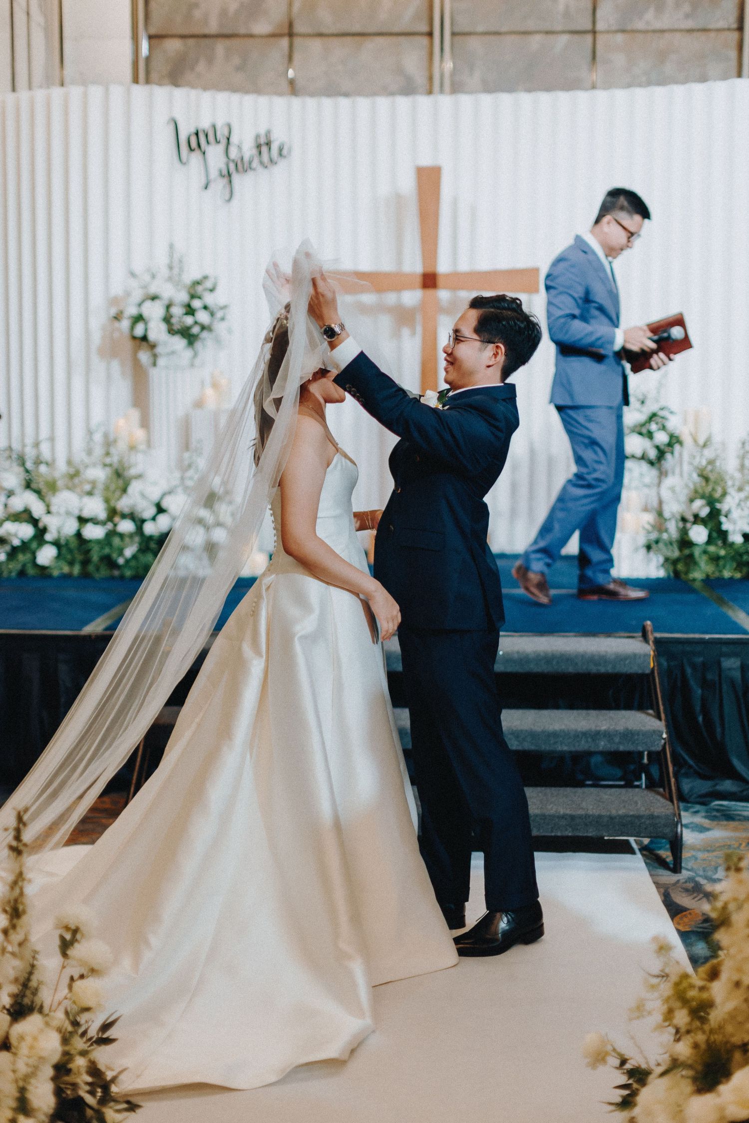 A celebratory moment during a wedding ceremony with white decor and floral arrangements.