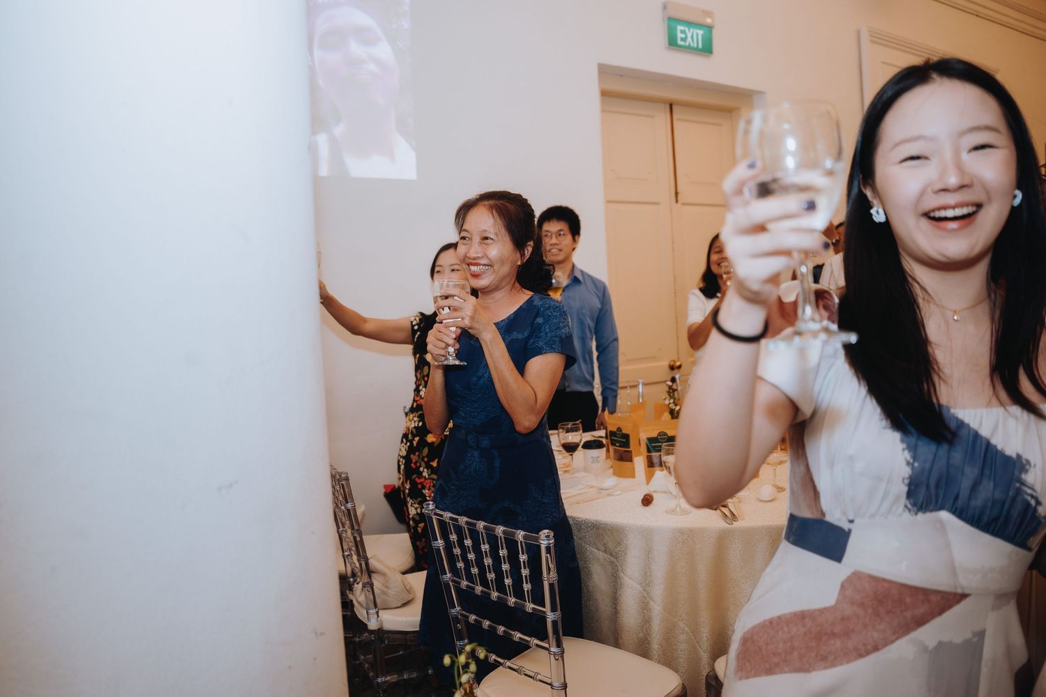 Wedding guests laughing and raising champagne glasses in a toast at a reception.