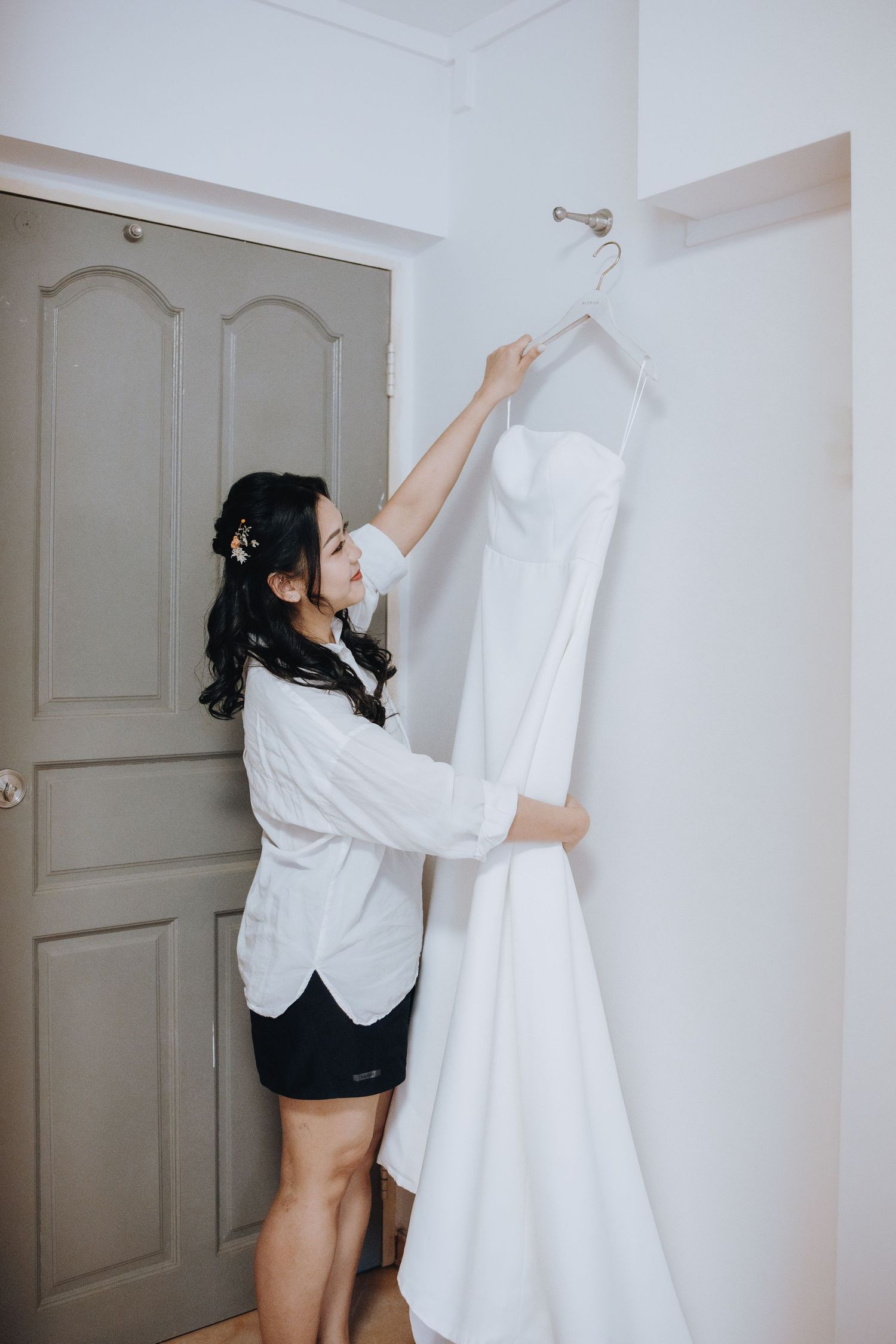 Bride preparing for wedding day, carefully taking white strapless gown off hanger in bright room.