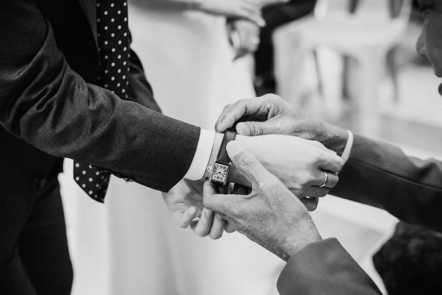 A black and white close-up of hands exchanging a wedding ring during a marriage ceremony.