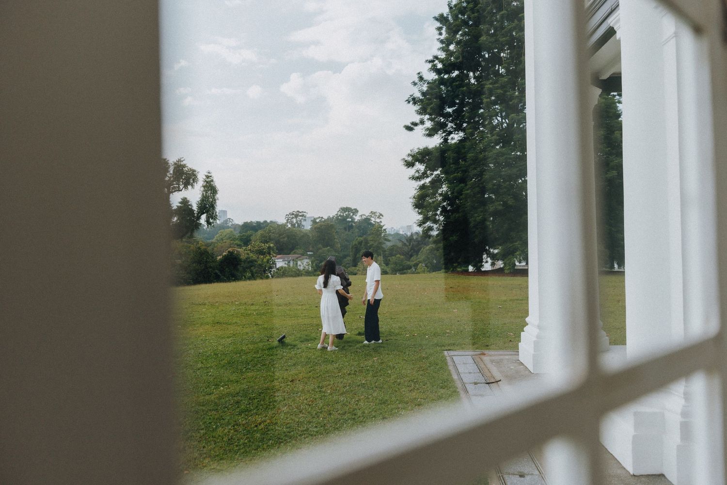 A couple stands on a grassy lawn viewed through a white architectural frame on a sunny day.