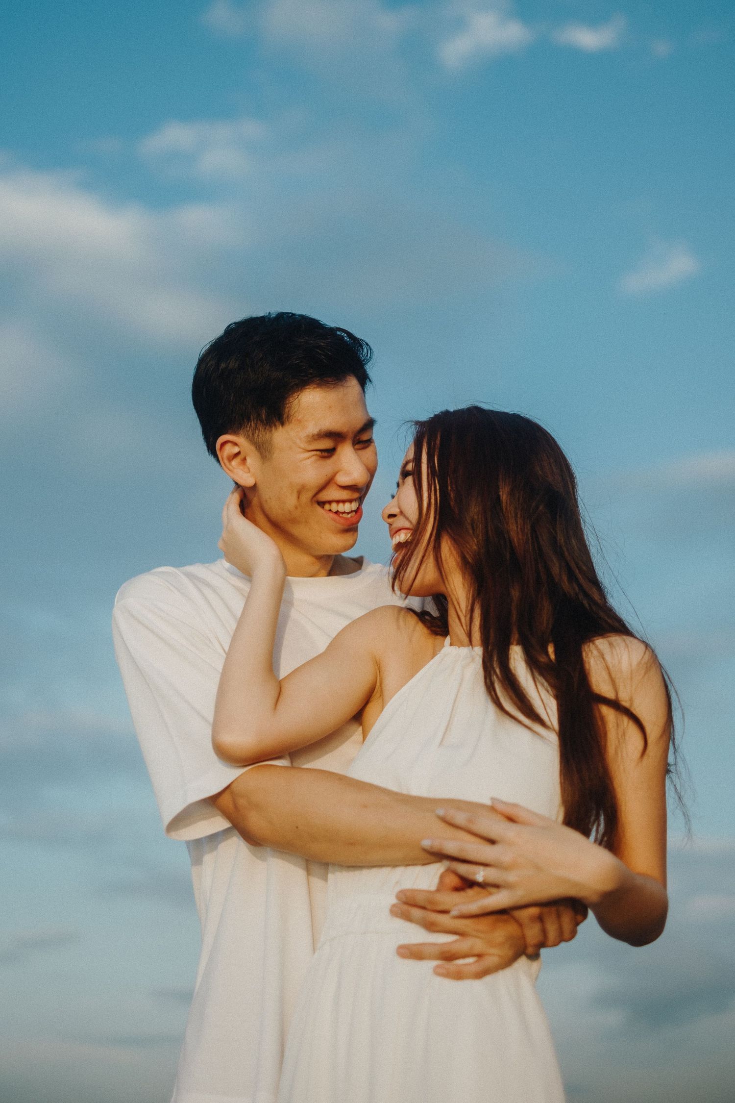 Couple laughing and embracing against blue sky background.