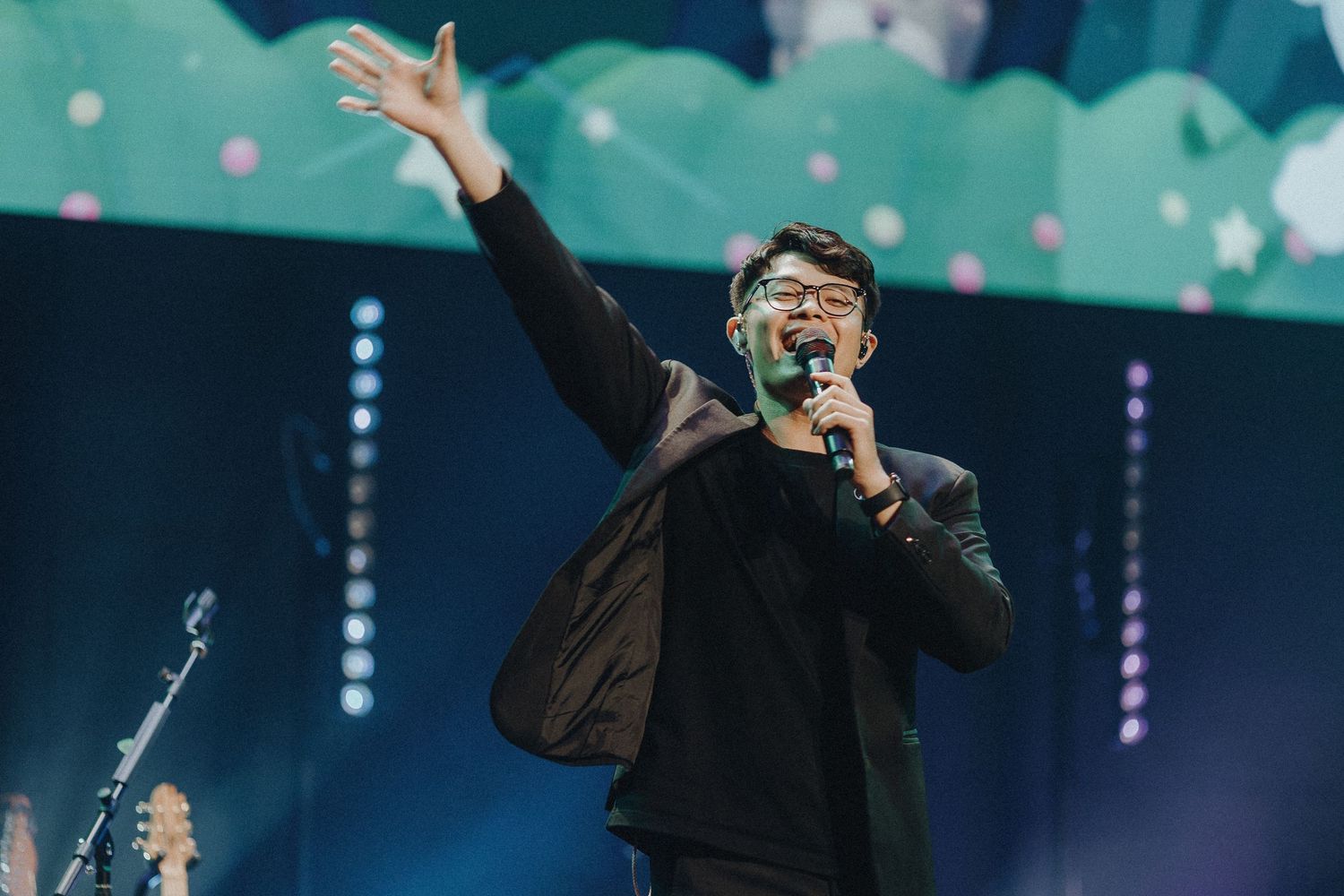 Concert performer on stage singing passionately with dramatic blue lighting and atmospheric effects.