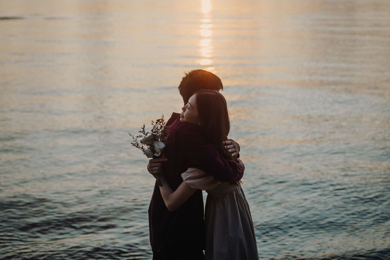 Silhouetted couple embracing near calm ocean waters at sunset.