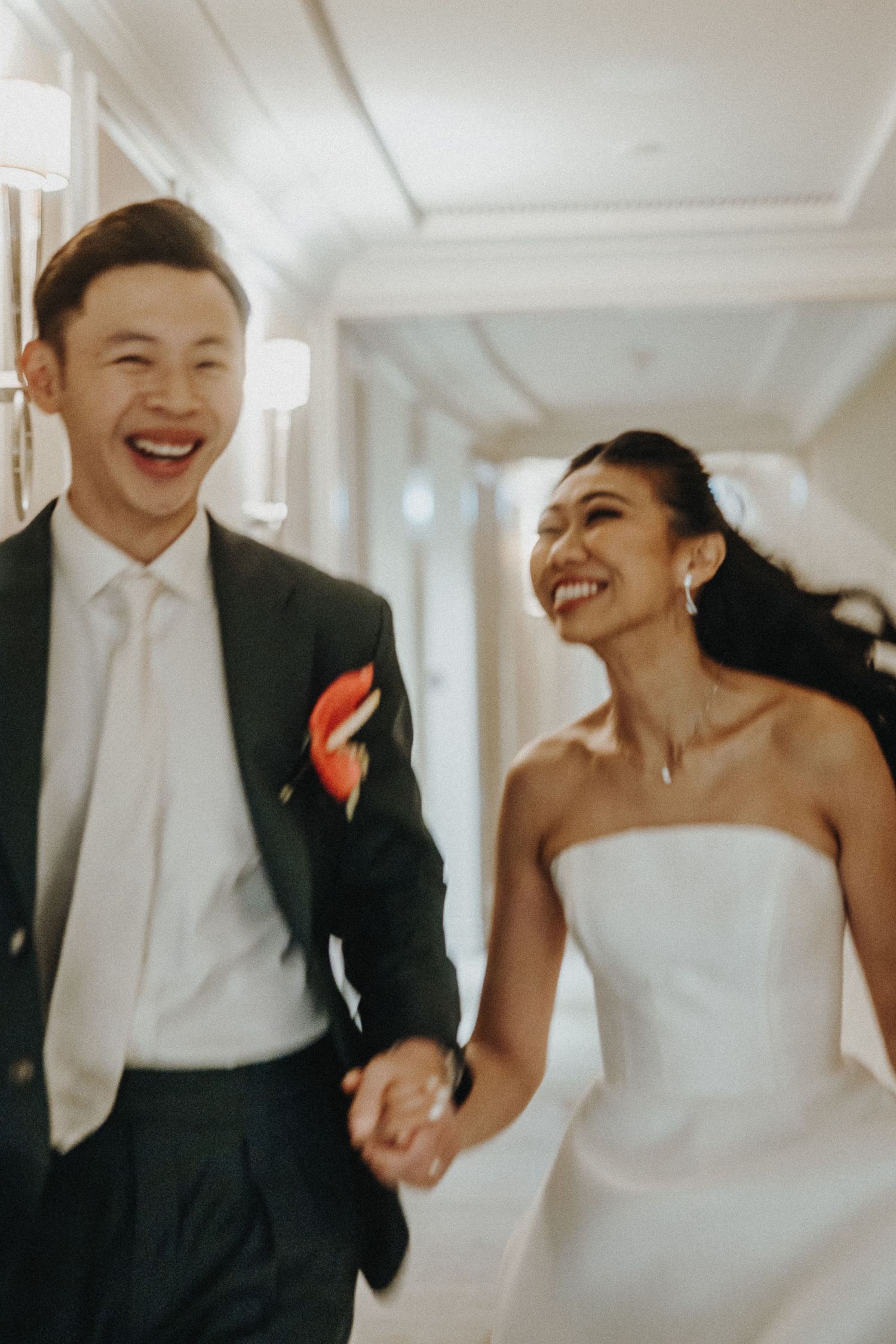 A joyful couple laughing together in an elegant white hallway.
