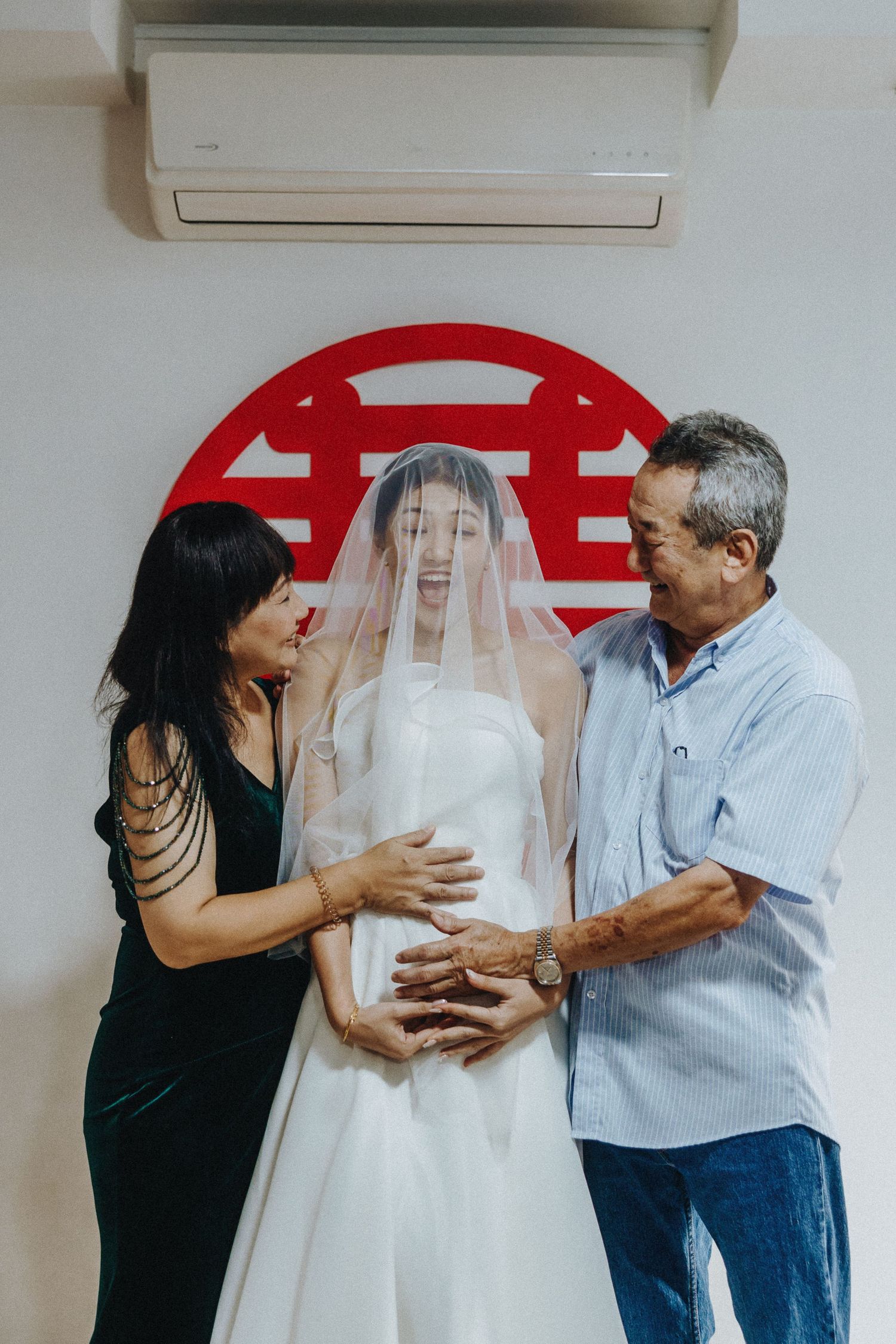 Wedding dress being adjusted and prepared in a room with red decorative elements on the wall.