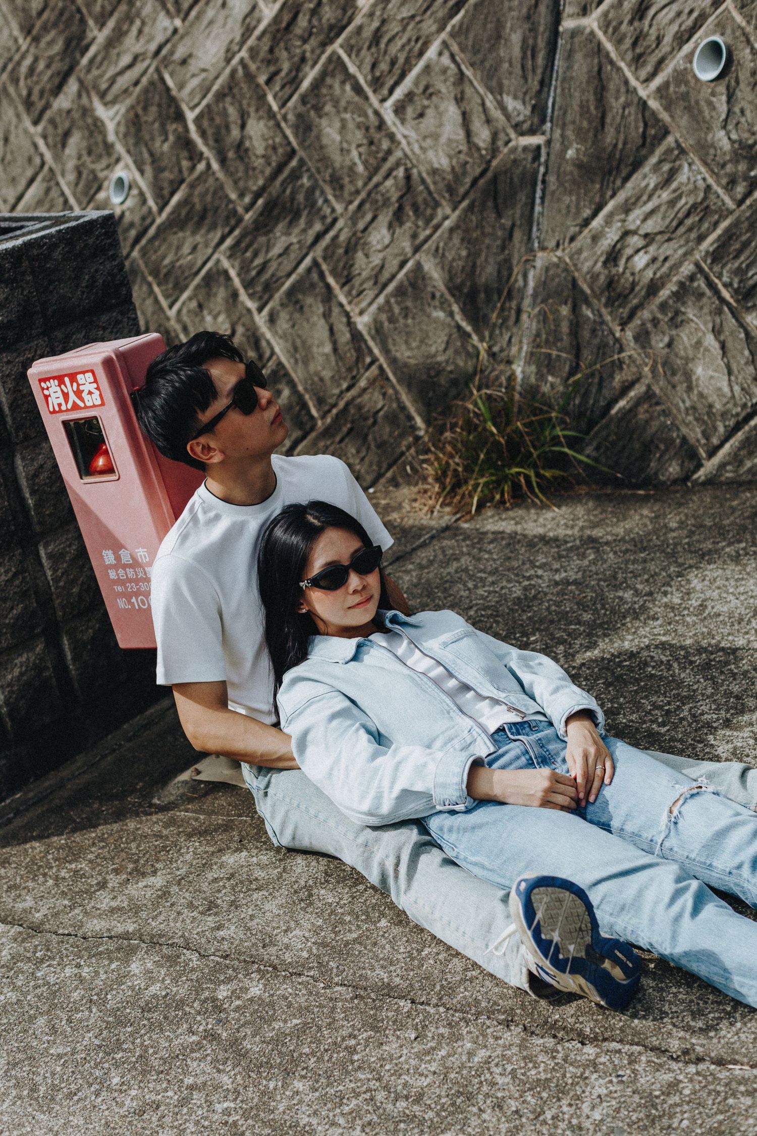 Casual outdoor photoshoot with subjects lounging on concrete surface wearing denim.