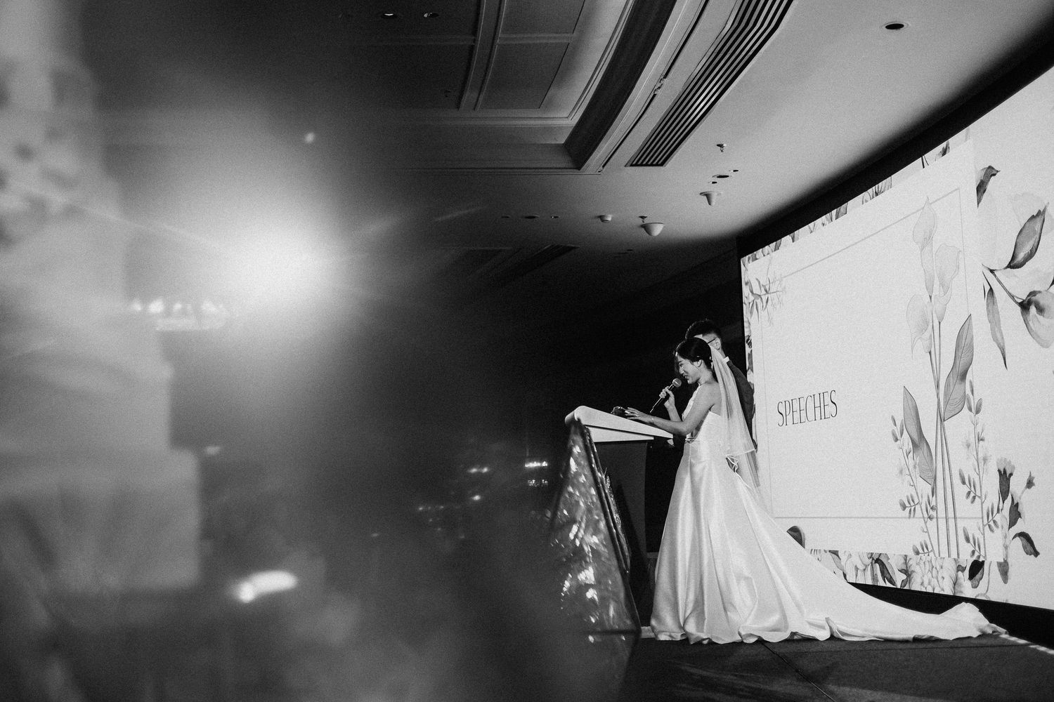 A dramatic black and white photo of a wedding reception with stage lighting effects.