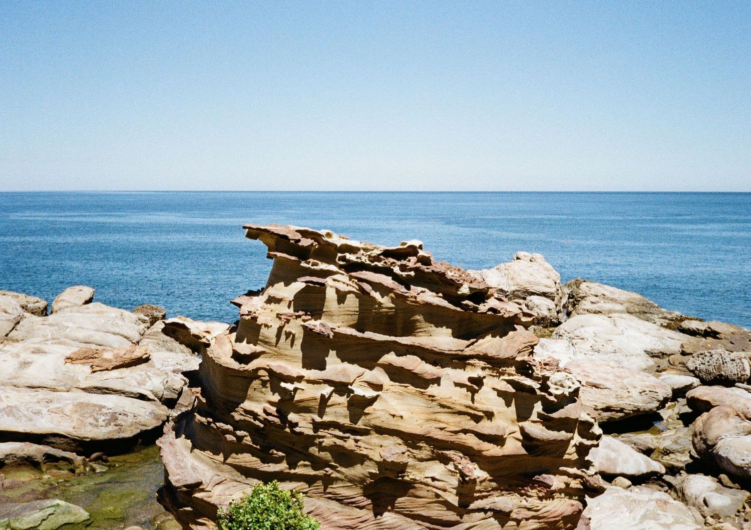 Rocky coastal landscape with jagged limestone formations stretching along the blue ocean shoreline.