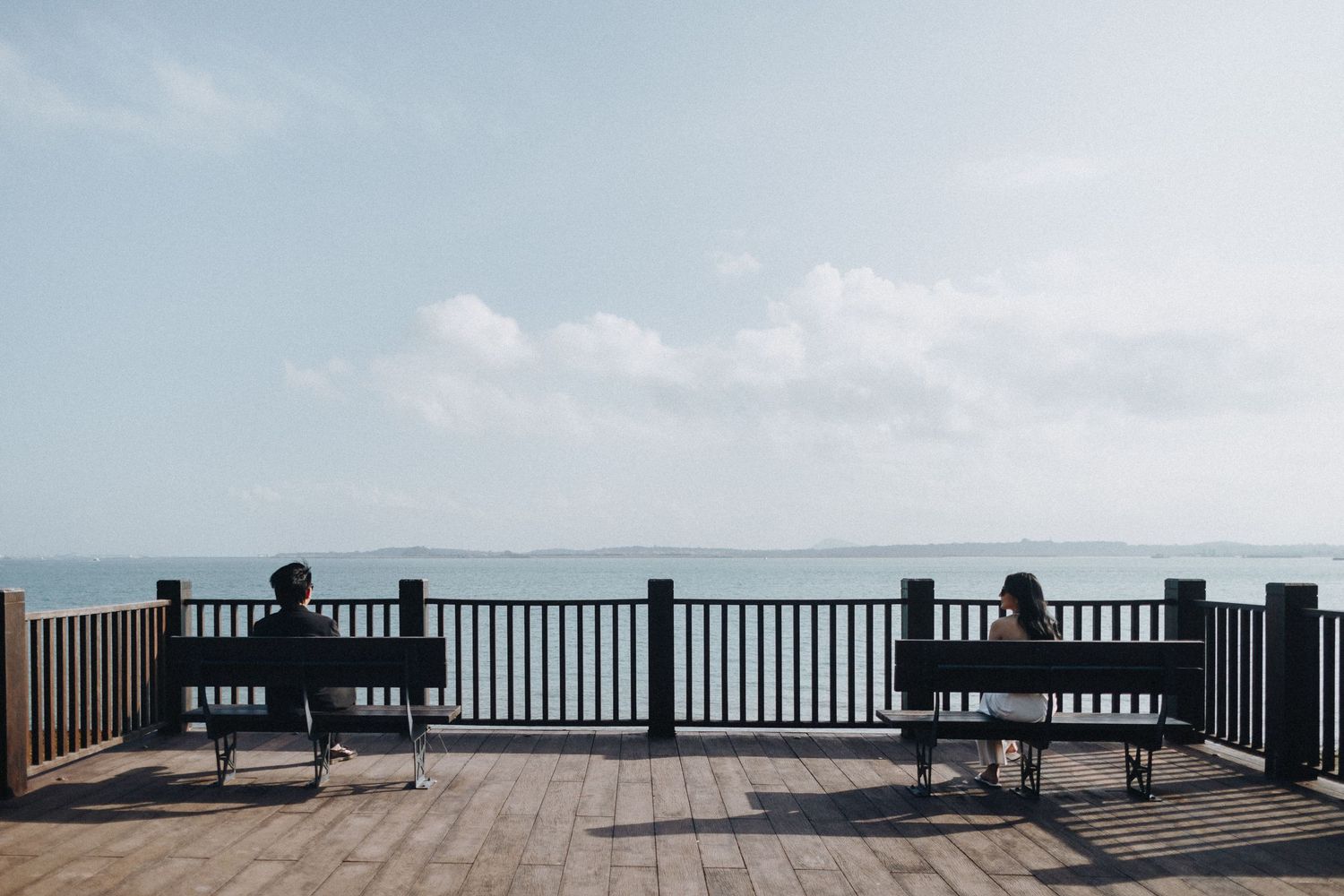 Row of empty benches overlooking a scenic ocean view with cloudy sky.