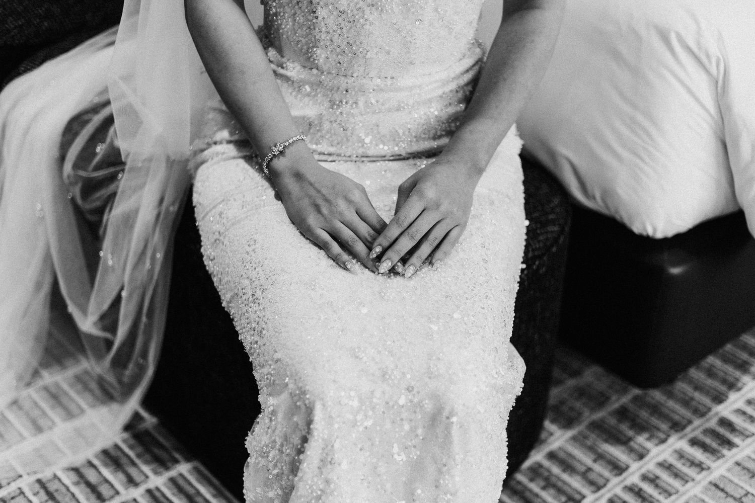 Black and white image showing the intricate lace details of a wedding dress with hands gently folded in the lap.