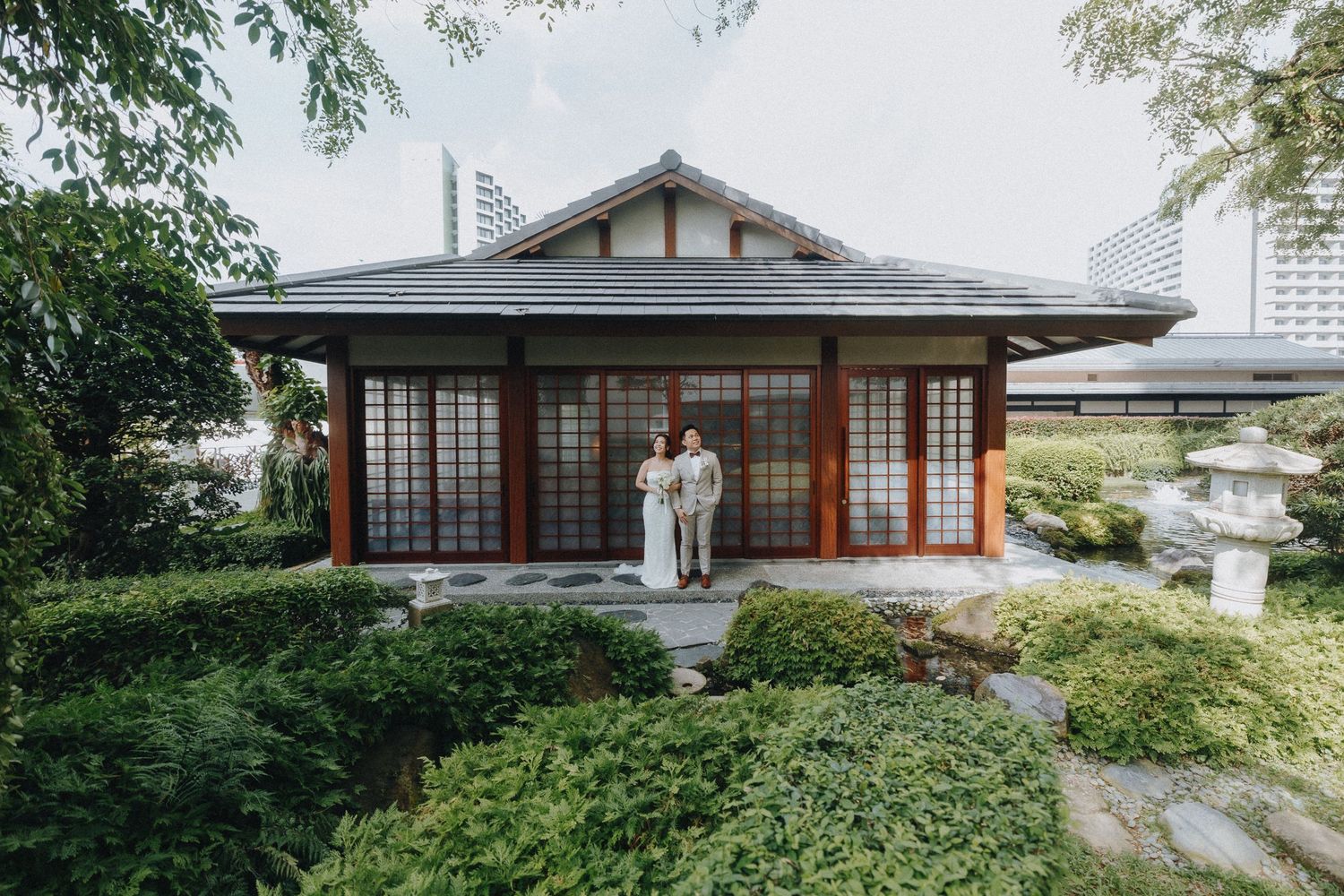 Traditional Japanese pavilion surrounded by manicured garden and modern buildings.