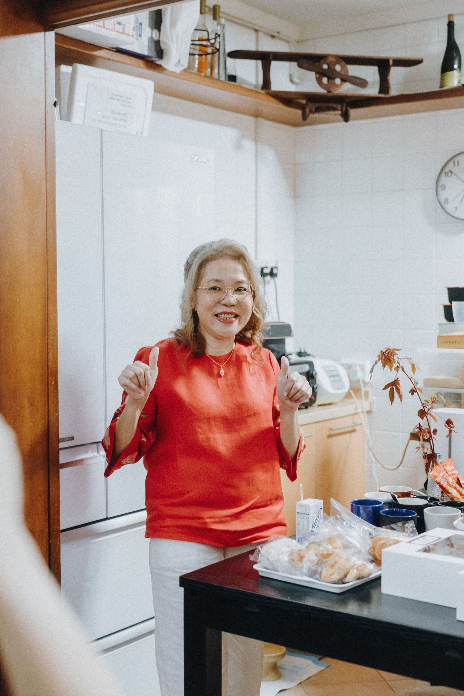A person in a bright red sweater laughs joyfully while sitting at a table in an indoor setting.