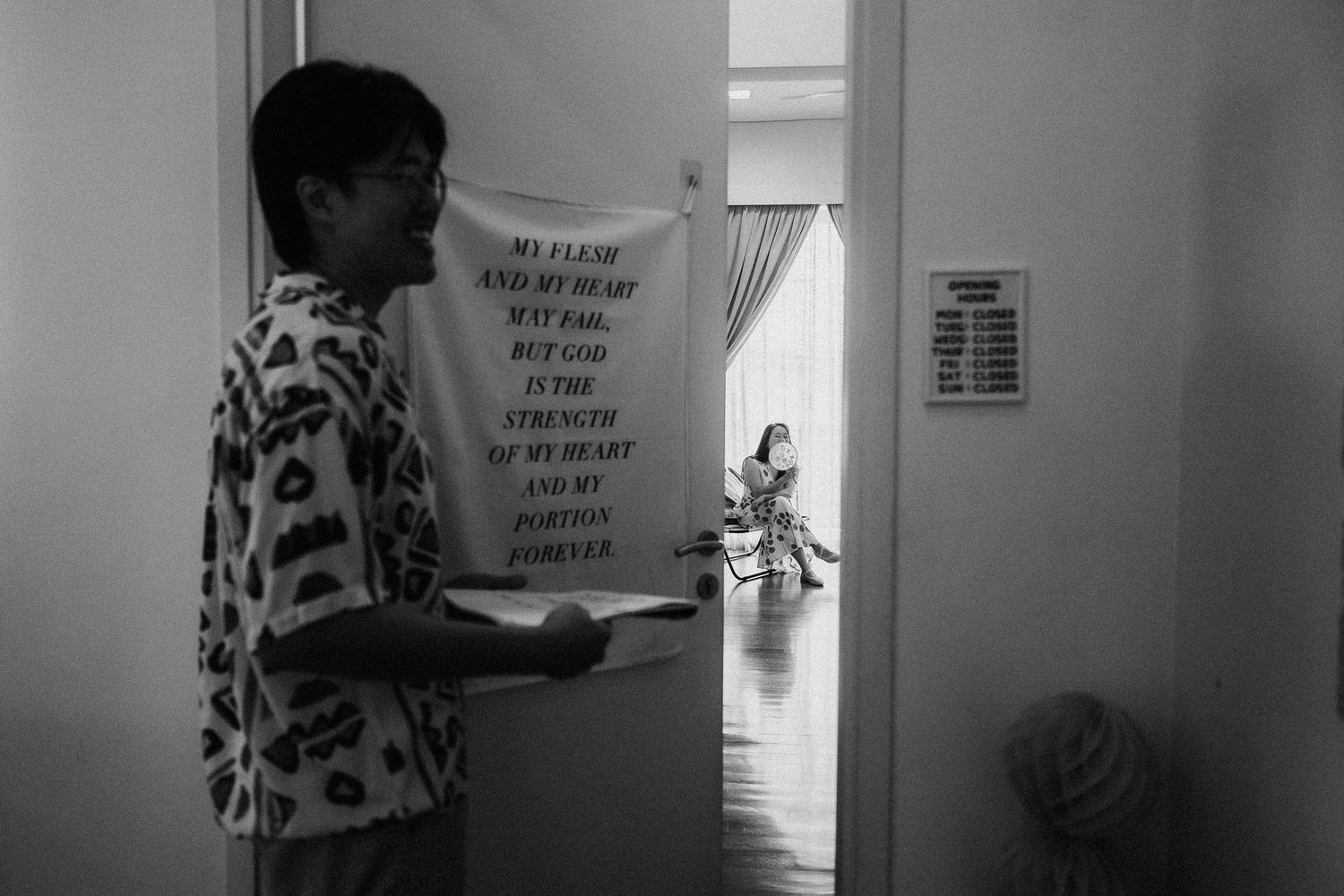 A person in a leopard print shirt reads a sign posted on a door in black and white photography.