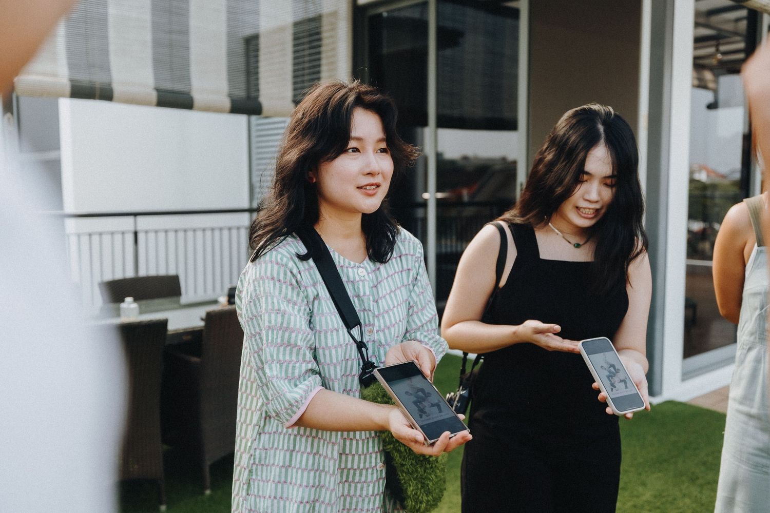 Two women stand together outdoors looking at something on a mobile device.