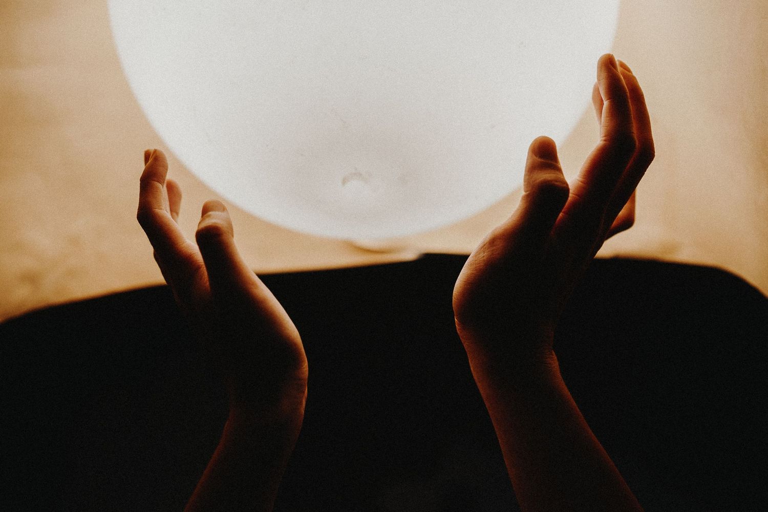 Silhouetted hands reaching up toward glowing light against dark background.