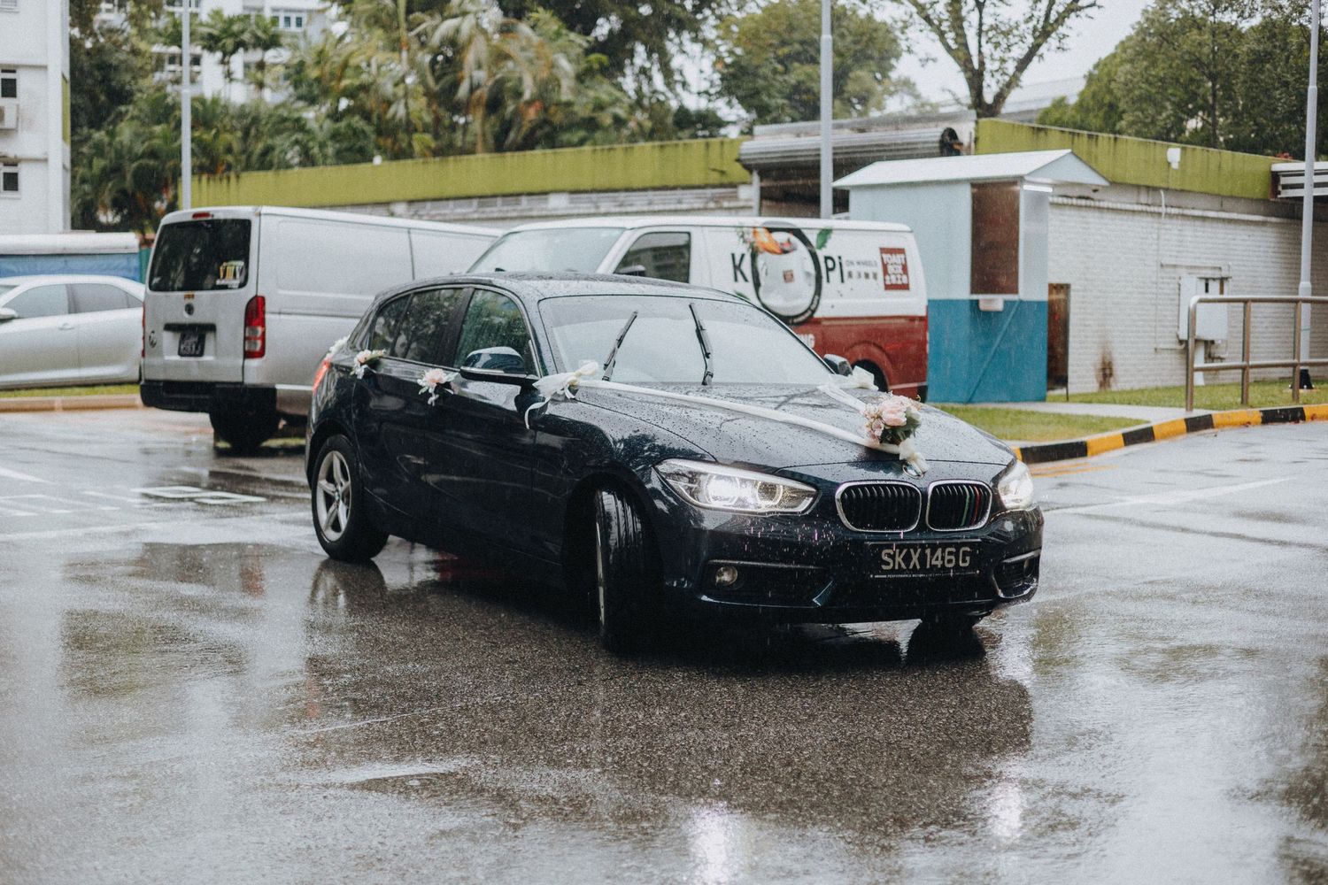 Cars parked in a rainy parking lot with puddles reflecting the overcast sky.