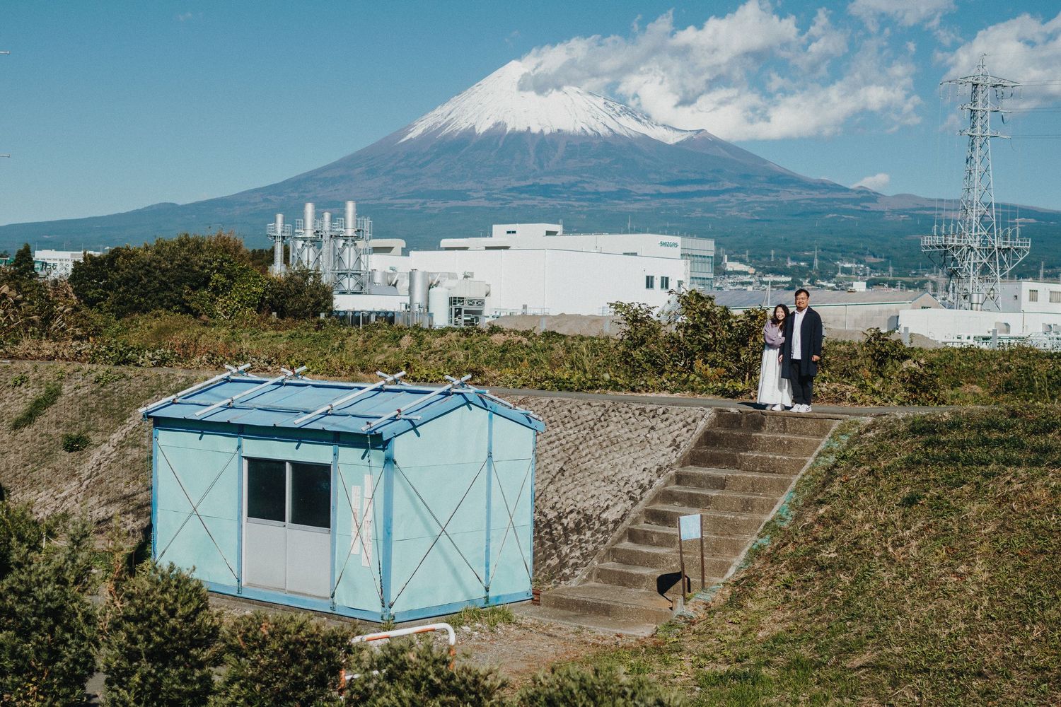 Mount Fuji rises majestically behind a blue storage unit and concrete steps.
