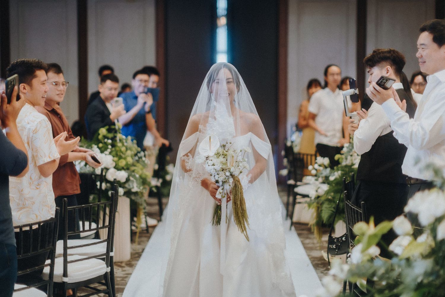 A wedding ceremony with guests watching as the bride walks down the aisle in a flowing veil.