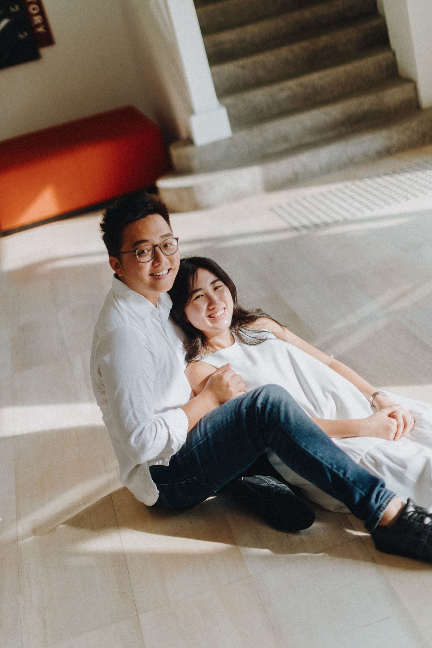 Couple relaxing and cuddling together on indoor stairs in casual white and denim outfits.