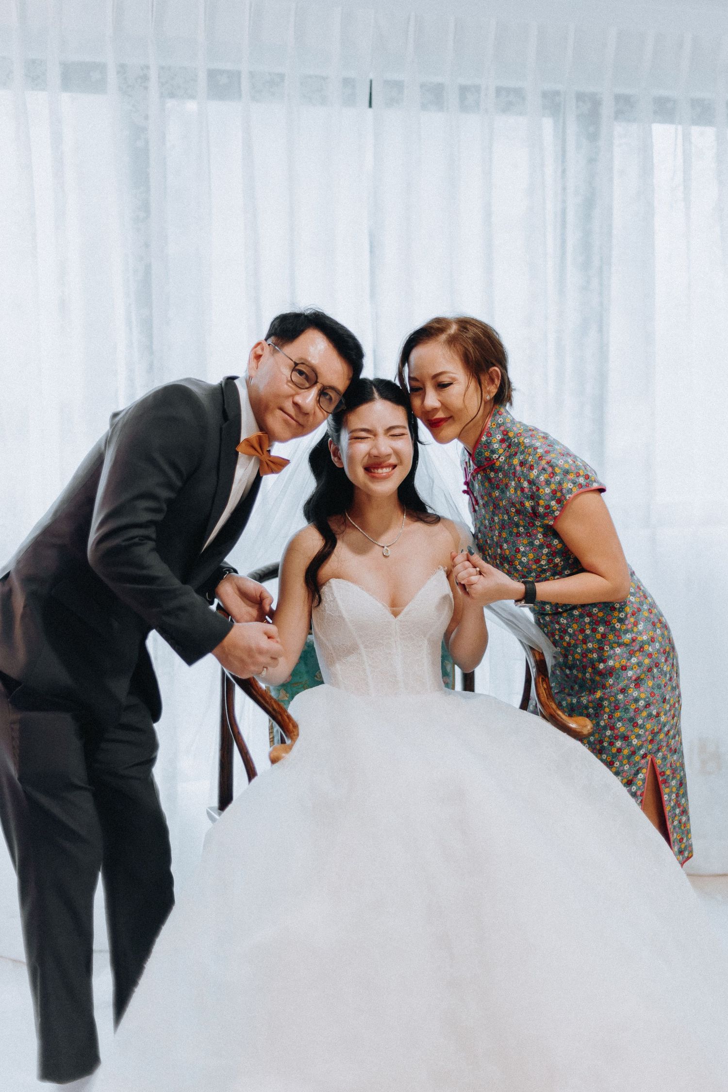 Smiling bride in white ballgown poses with two guests at a bright wedding venue.