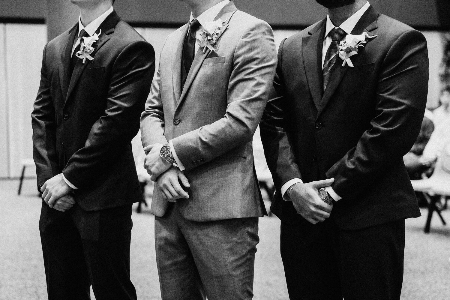 Three groomsmen in formal suits with boutonnieres stand together in a black and white photo.