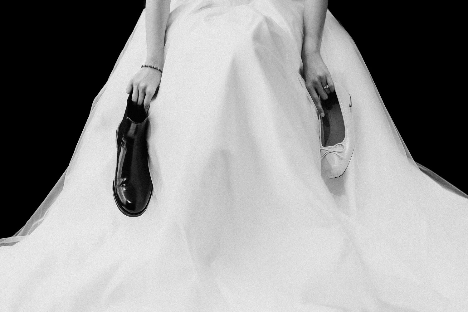 Black and white artistic photograph showing contrasting shoes held against a white flowing fabric background.