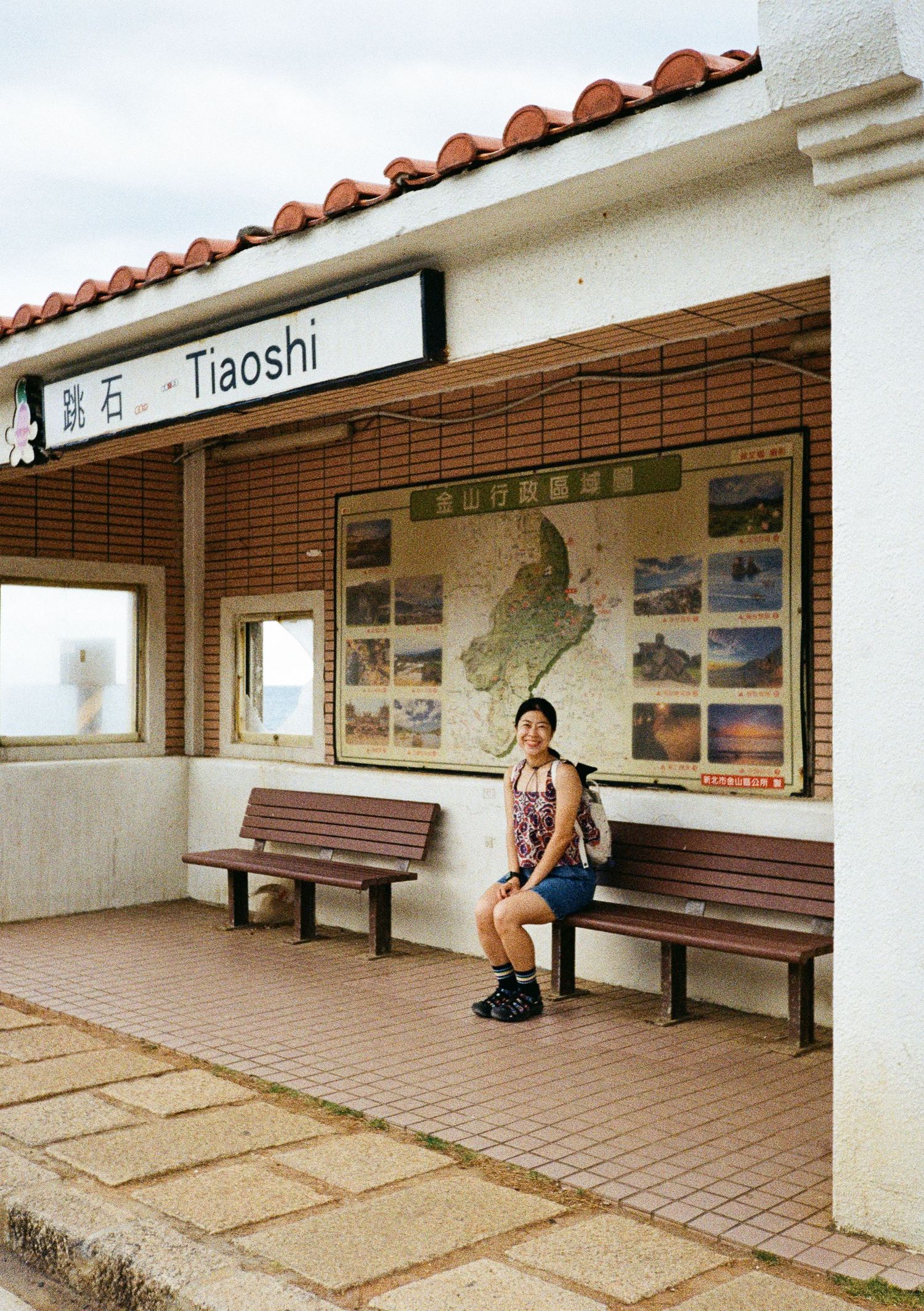 Empty train station platform with benches and travel information boards mounted on wall.