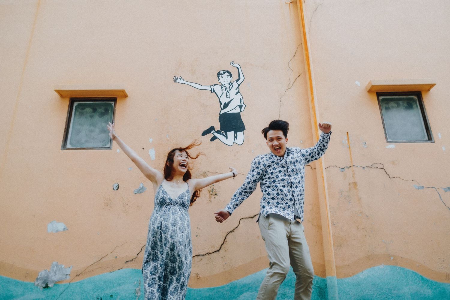 Couple in coordinated outfits strikes fun poses against a peach-colored wall backdrop.