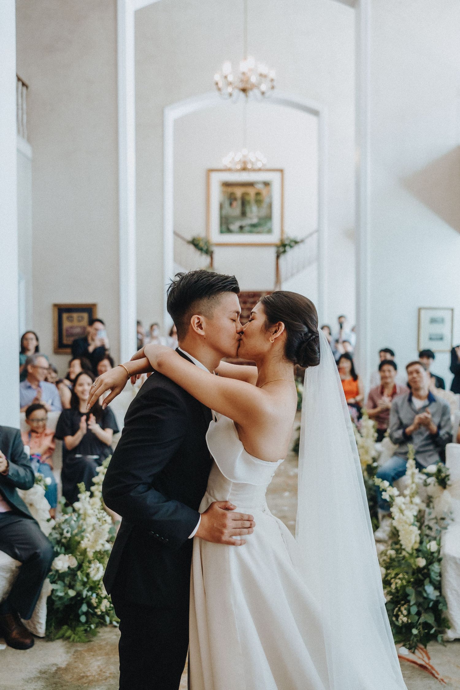 A wedding ceremony kiss in an elegant white chapel filled with guests and floral decorations.