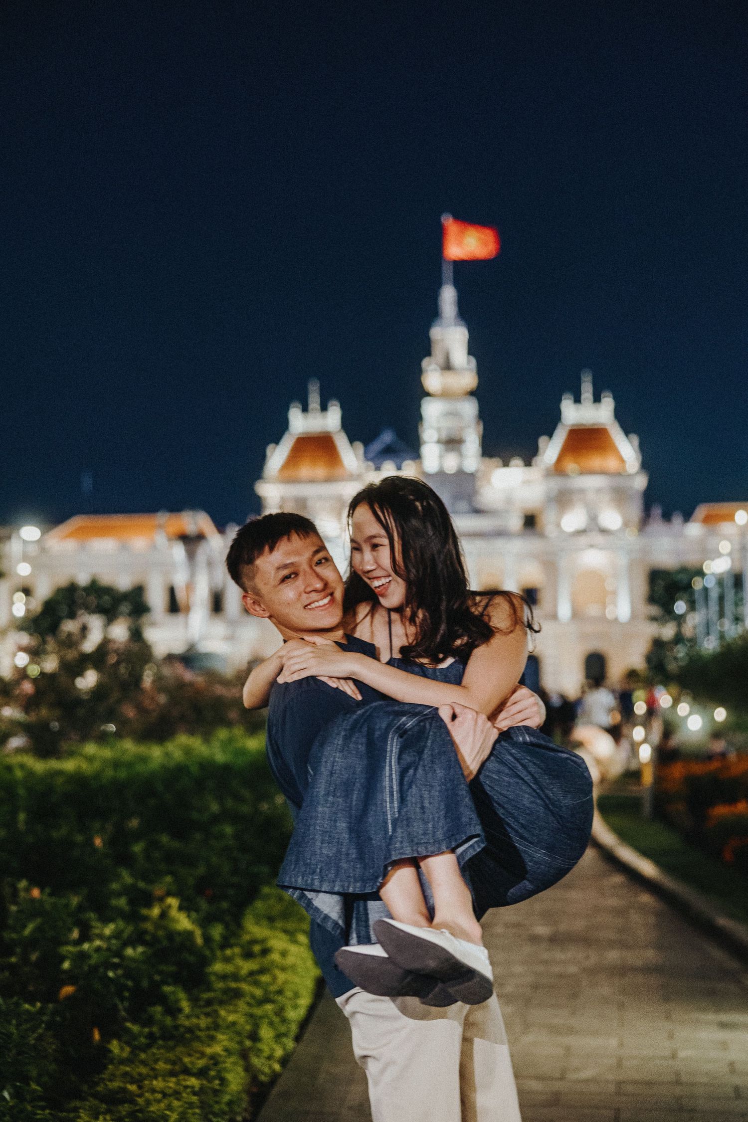 A romantic nighttime couple portrait taken in front of the illuminated Ho Chi Minh City Hall in Vietnam.