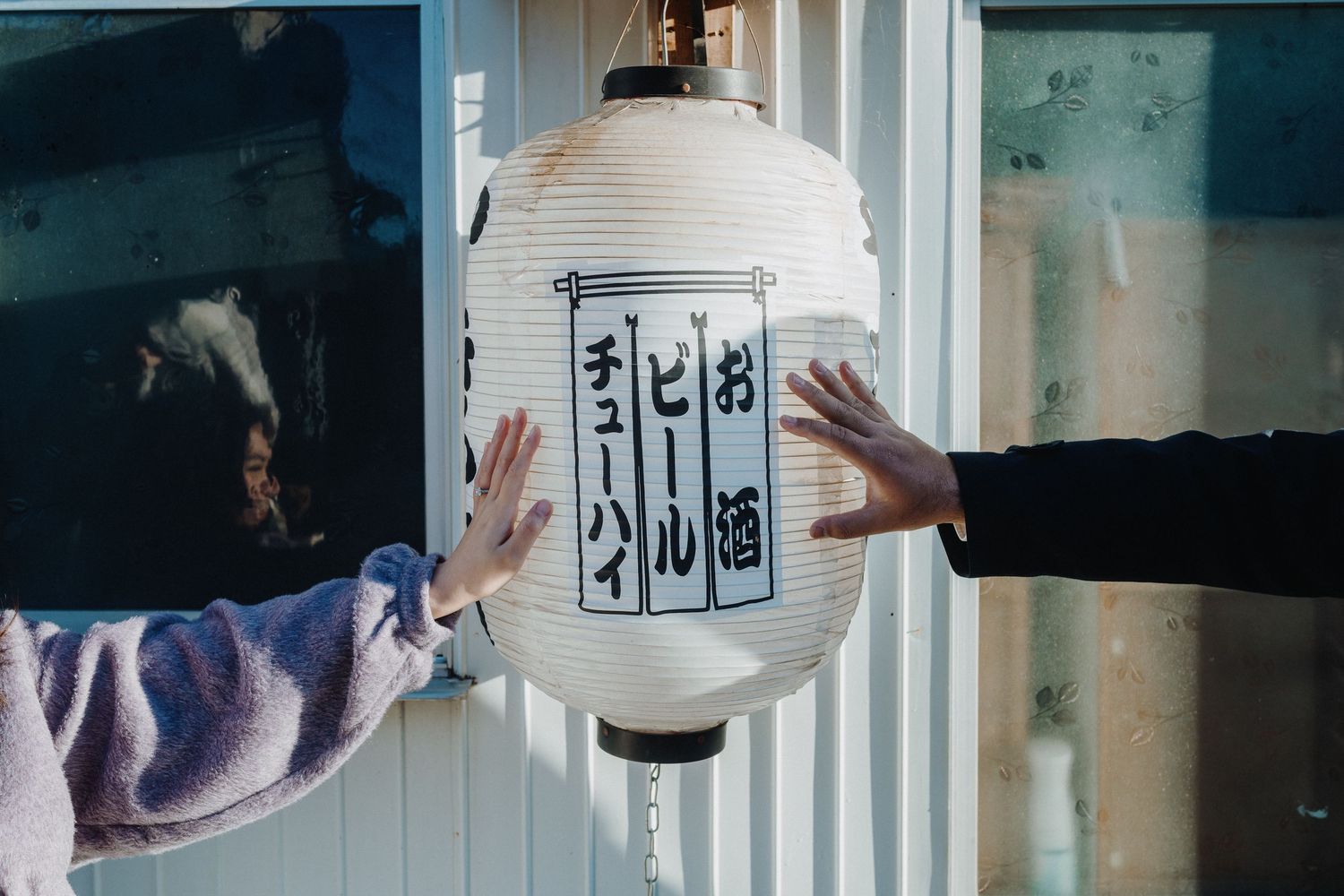 Hands reaching to touch traditional Japanese paper lantern with calligraphy.