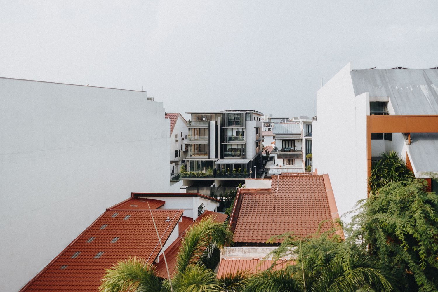Wide panoramic view of a residential roofline with terracotta tiles and white buildings against a cloudy sky.