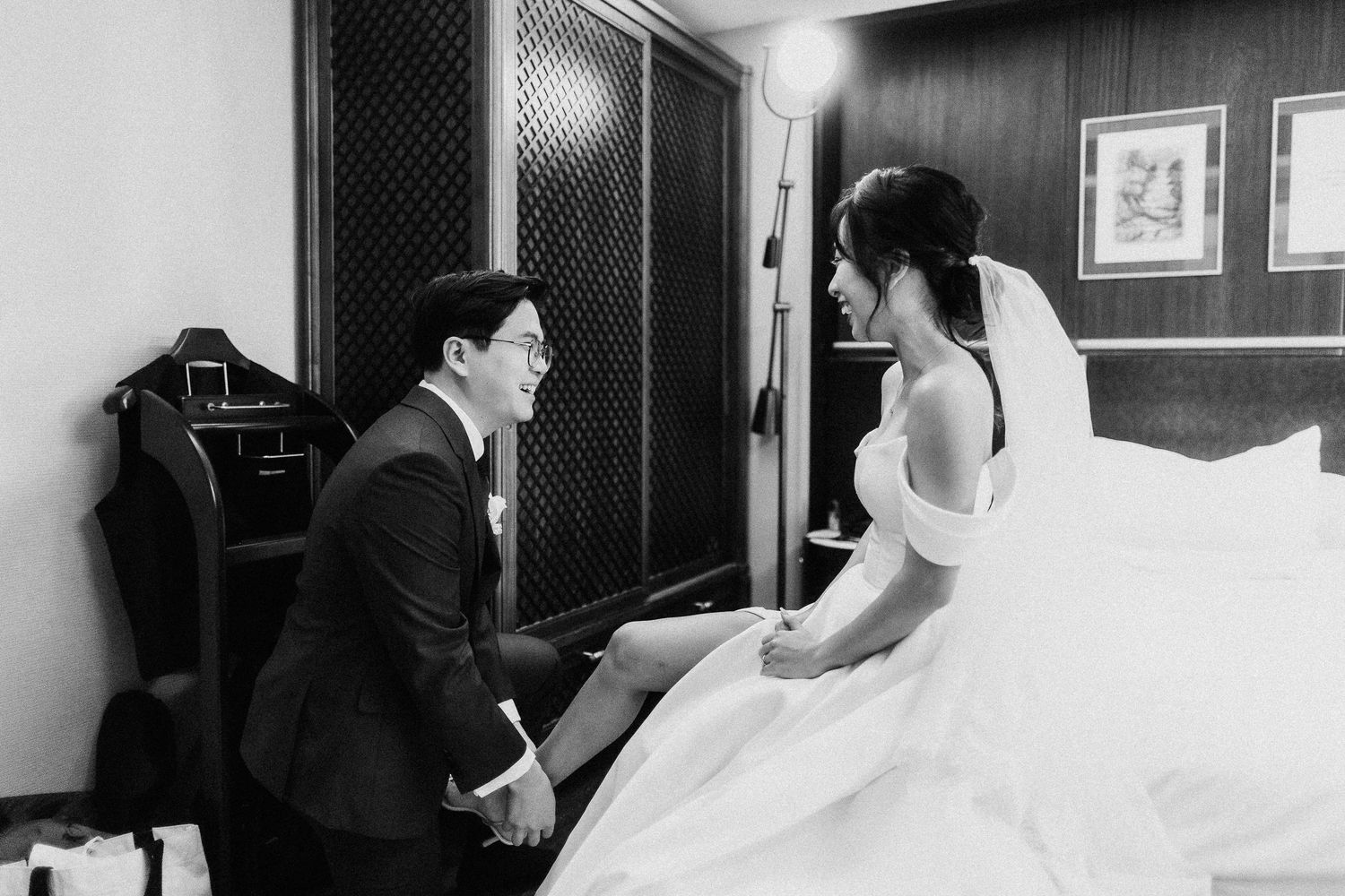 A black and white photograph of a couple sharing a joyful moment in a room before their wedding ceremony.