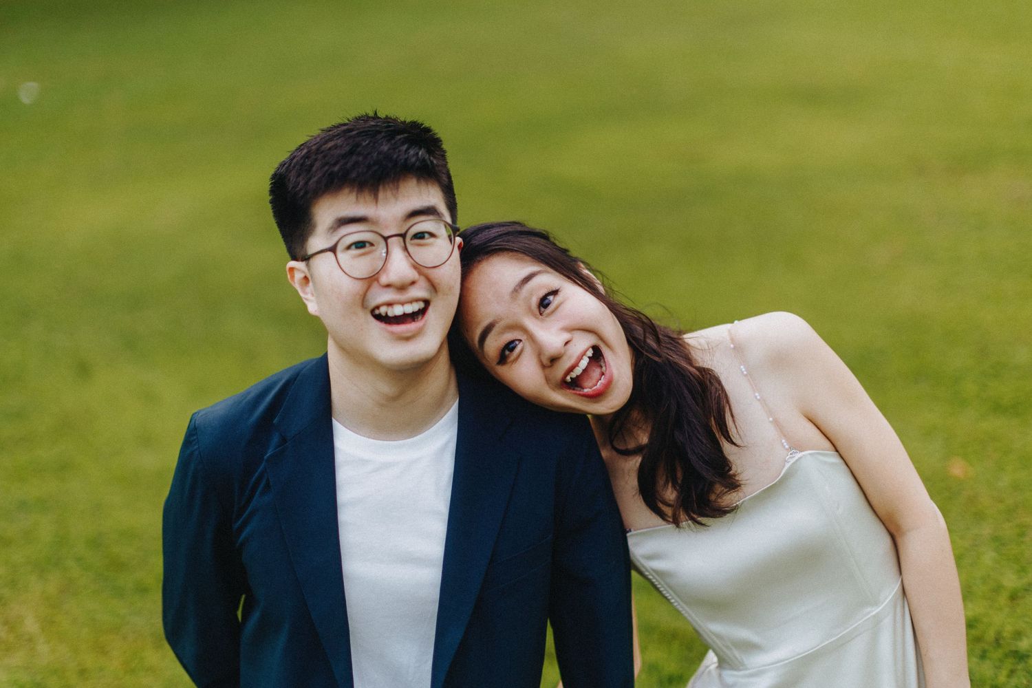 A happy couple smiles joyfully together on a sunny day with a green lawn in the background.