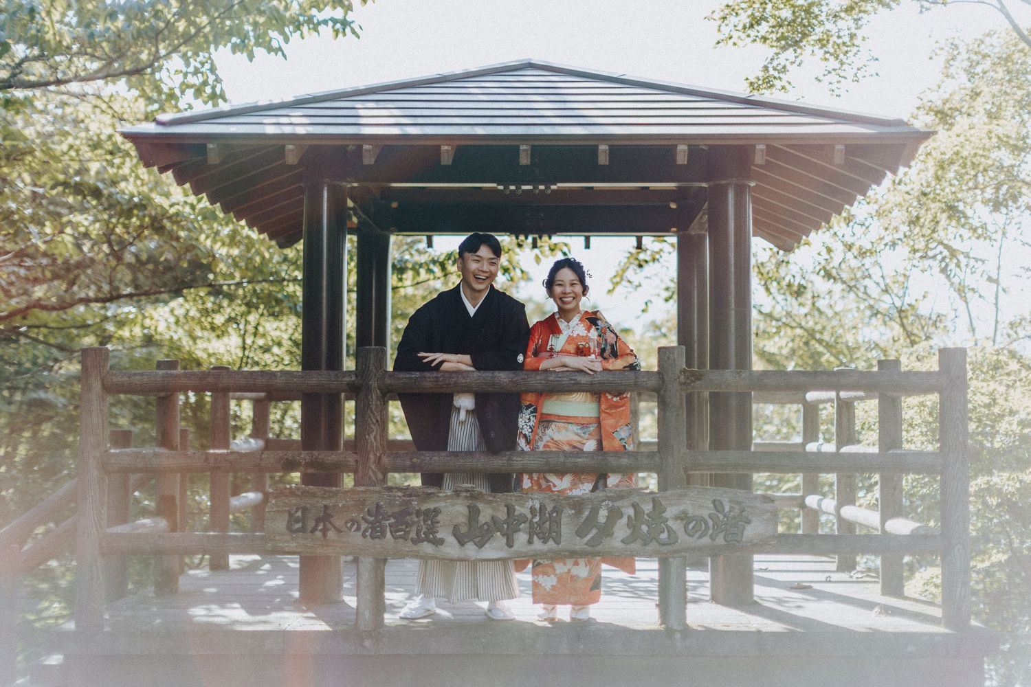 A traditional wooden gazebo sits in a park surrounded by autumn trees and provides shelter to visitors.