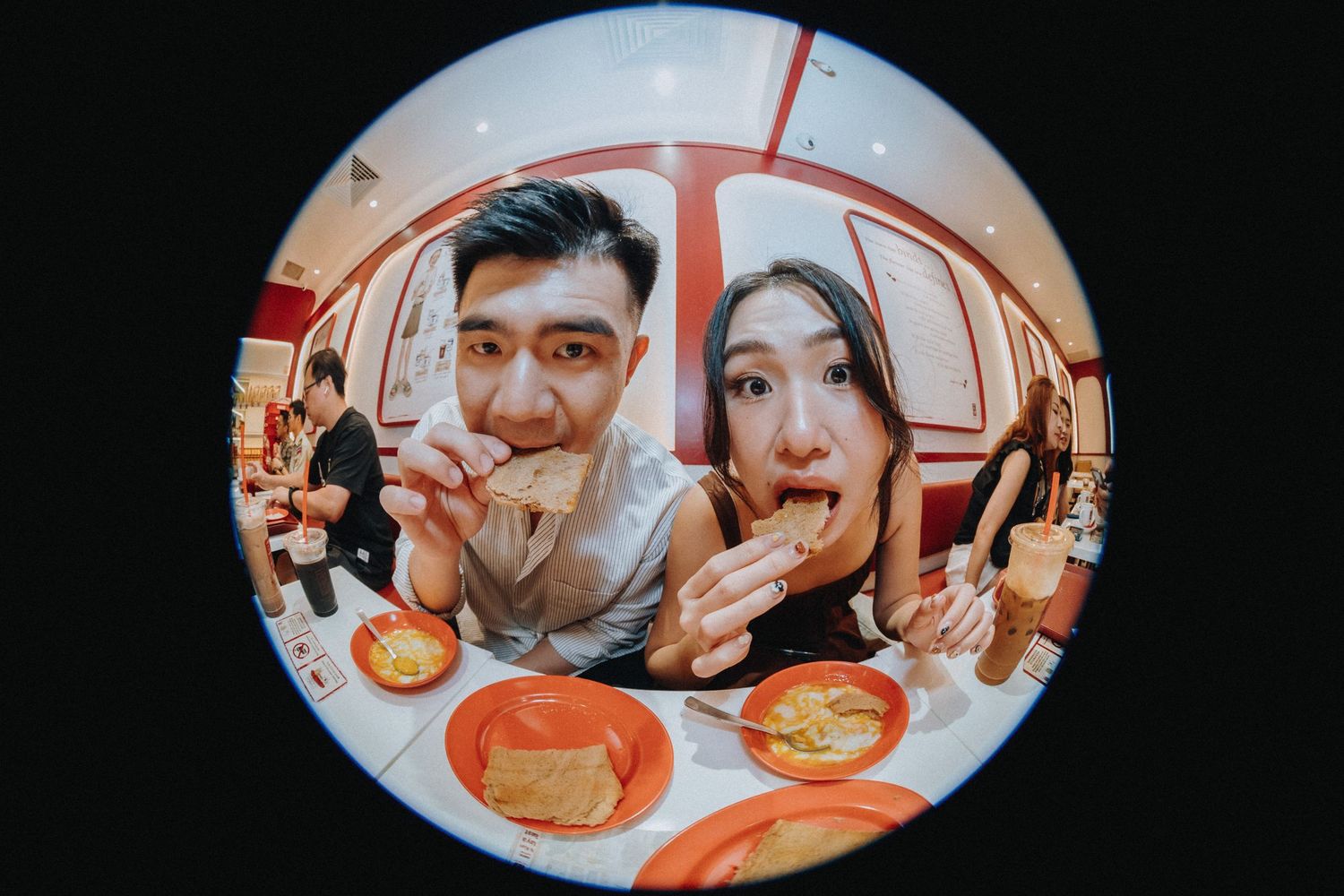 Couple eating food together captured through a fisheye lens in a bright restaurant setting.