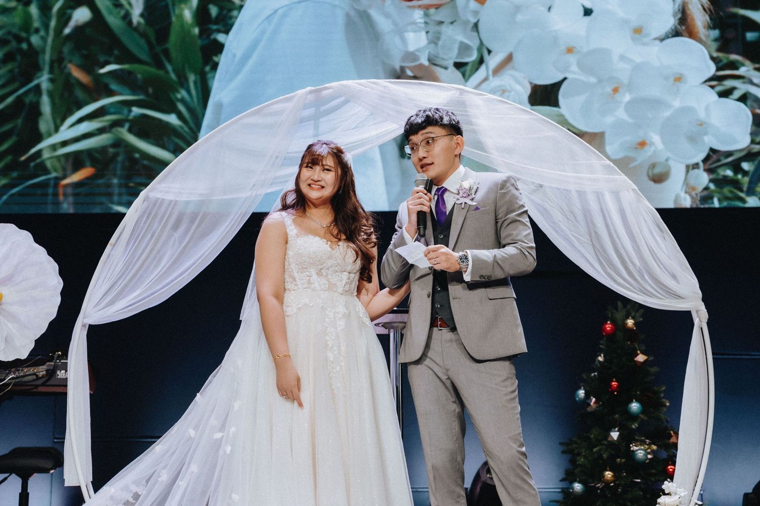 Wedding ceremony space decorated with white fabric arch and floral arrangements outdoors.