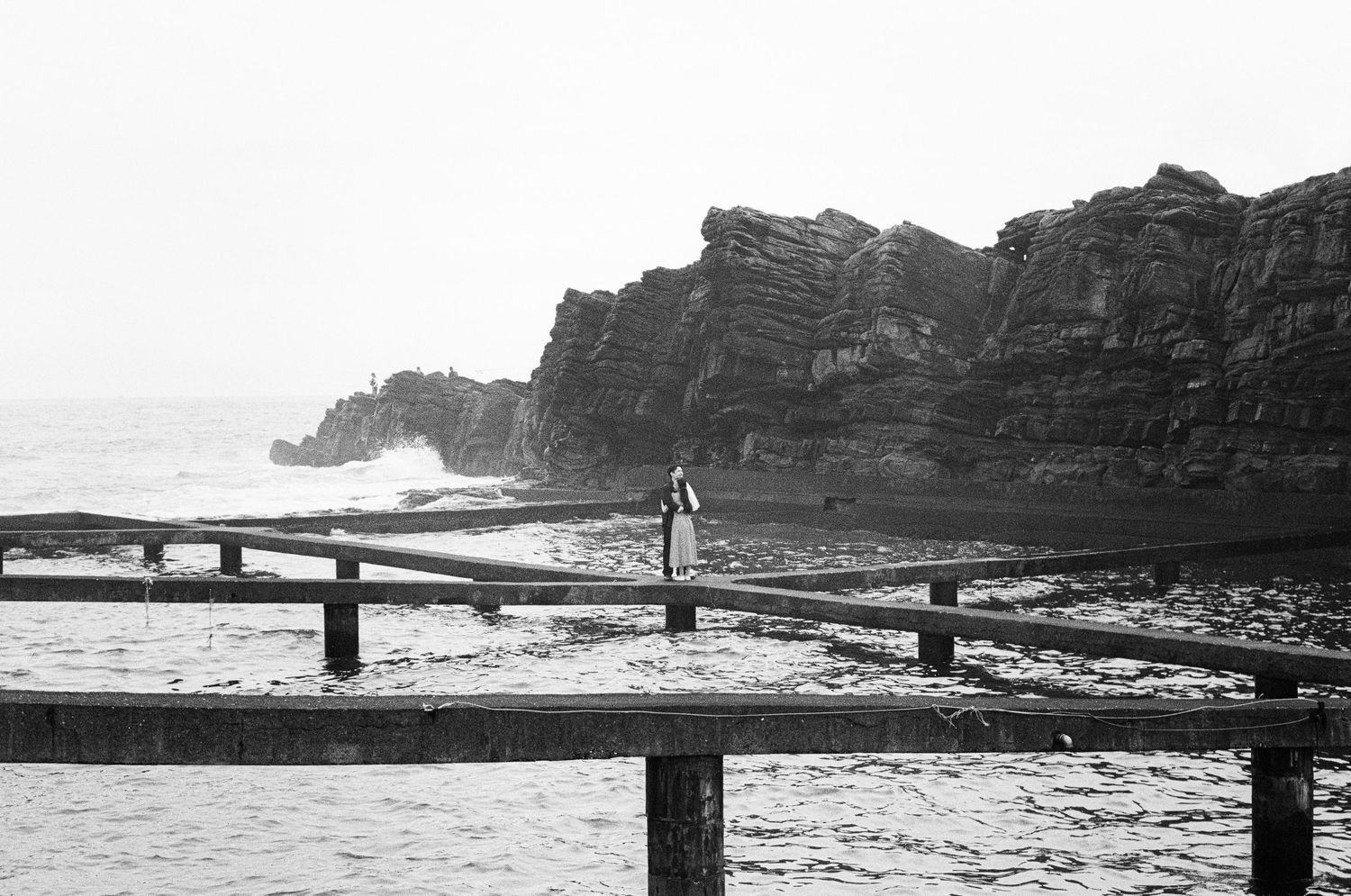 Black and white panoramic view of a rugged coastal landscape with cliffs and waves crashing against rocky shores.