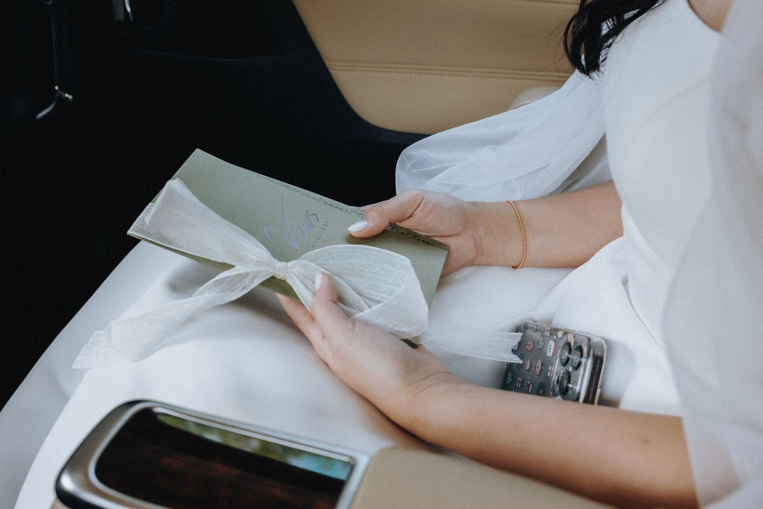 Bride in white dress reading a letter card while sitting in a luxury car on her wedding day.