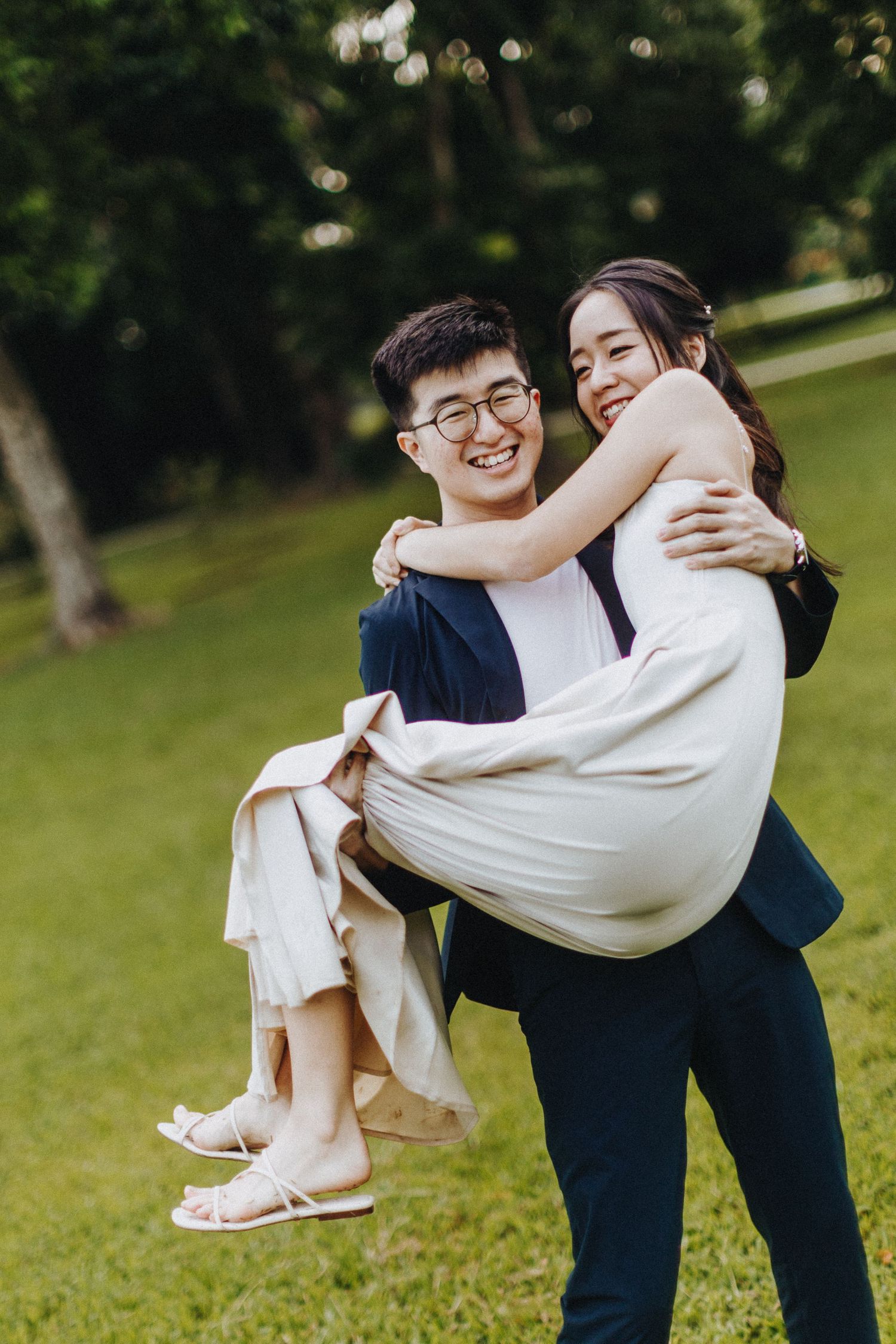 A joyful couple shares a playful moment as they embrace in a lush green garden setting.