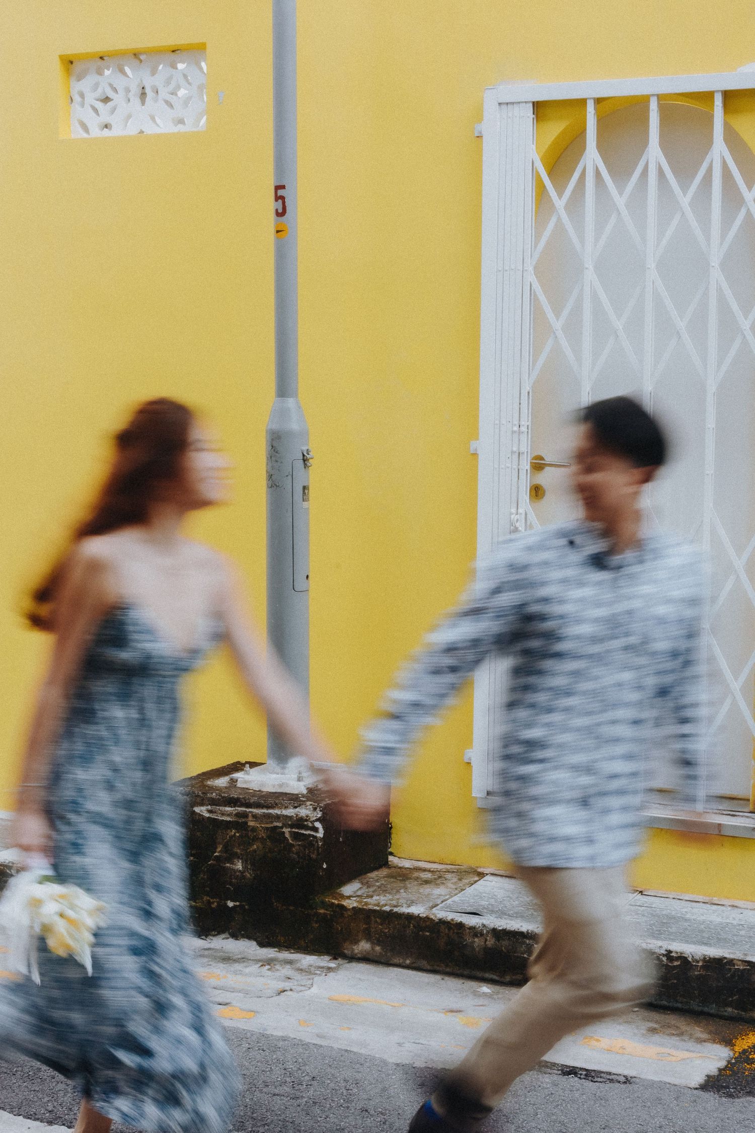 Motion blur sequence of person walking past yellow wall with white gate.