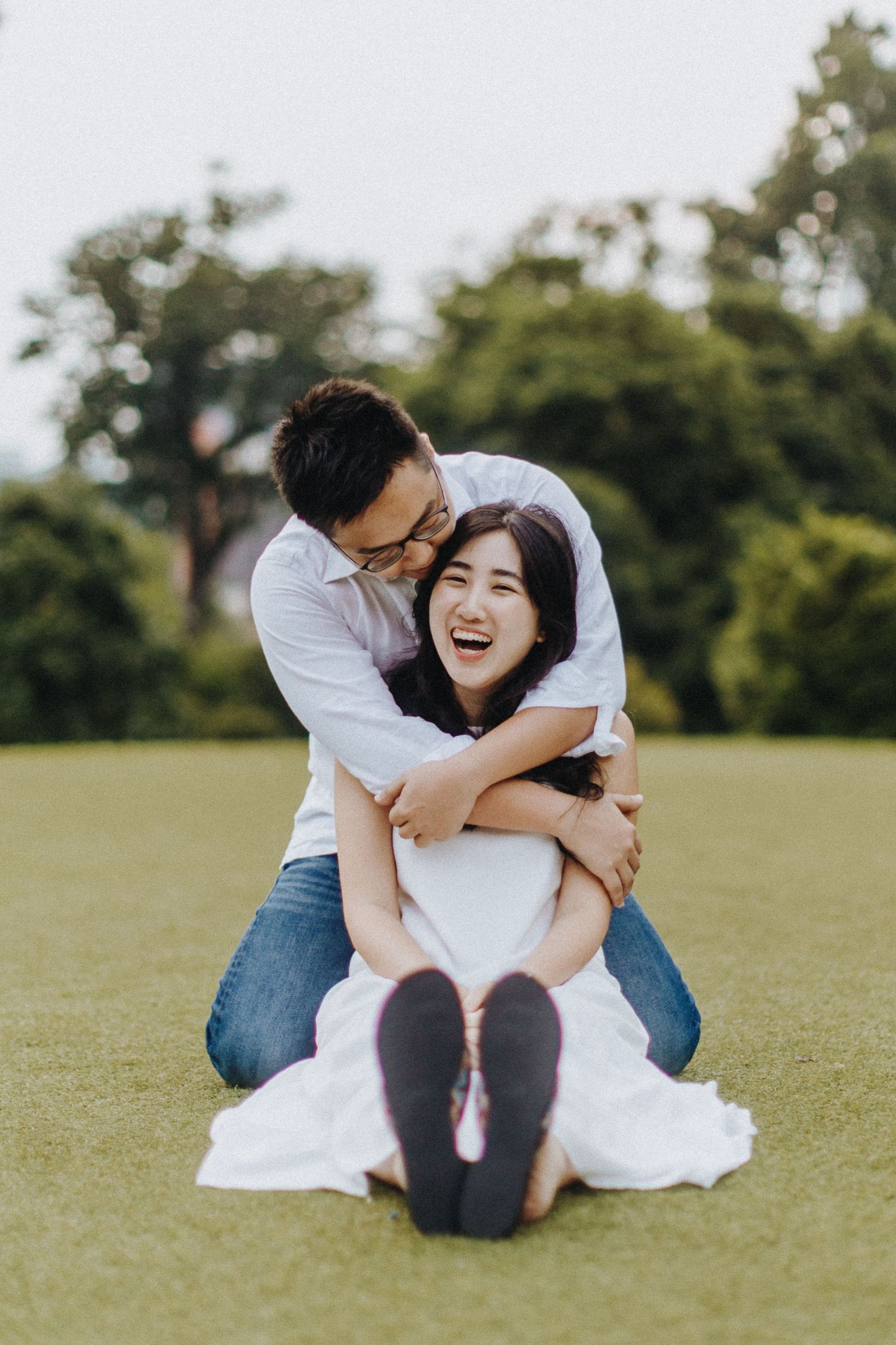 Candid couples photography session showing playful moments together on a grassy lawn in casual attire.