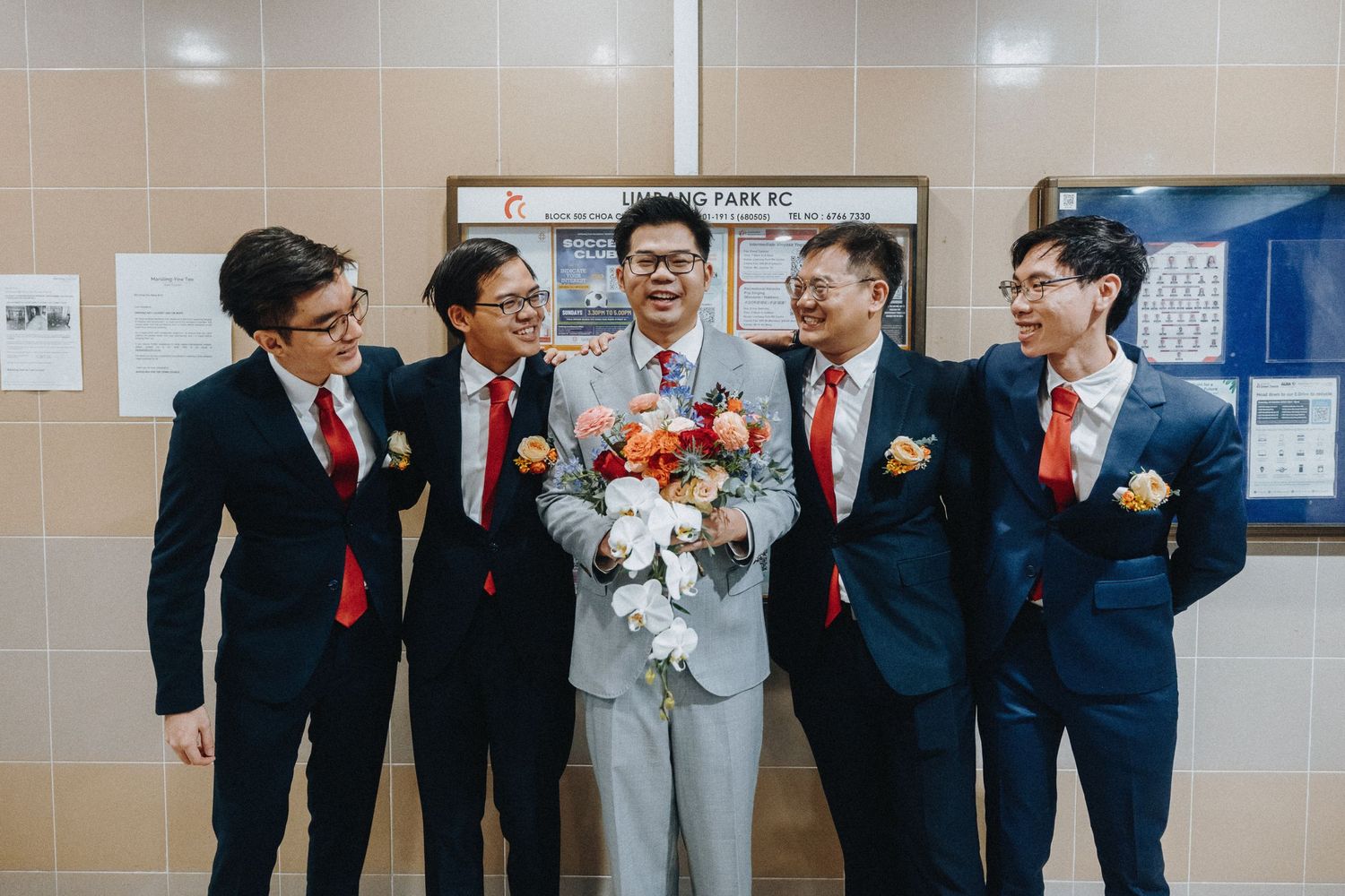 Wedding party members in dark suits share laughs and joyful moments during candid photo session in hallway.