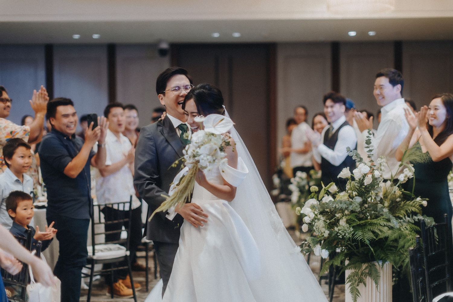 Celebration during a wedding ceremony in an elegant indoor venue with floral decorations and guests watching.