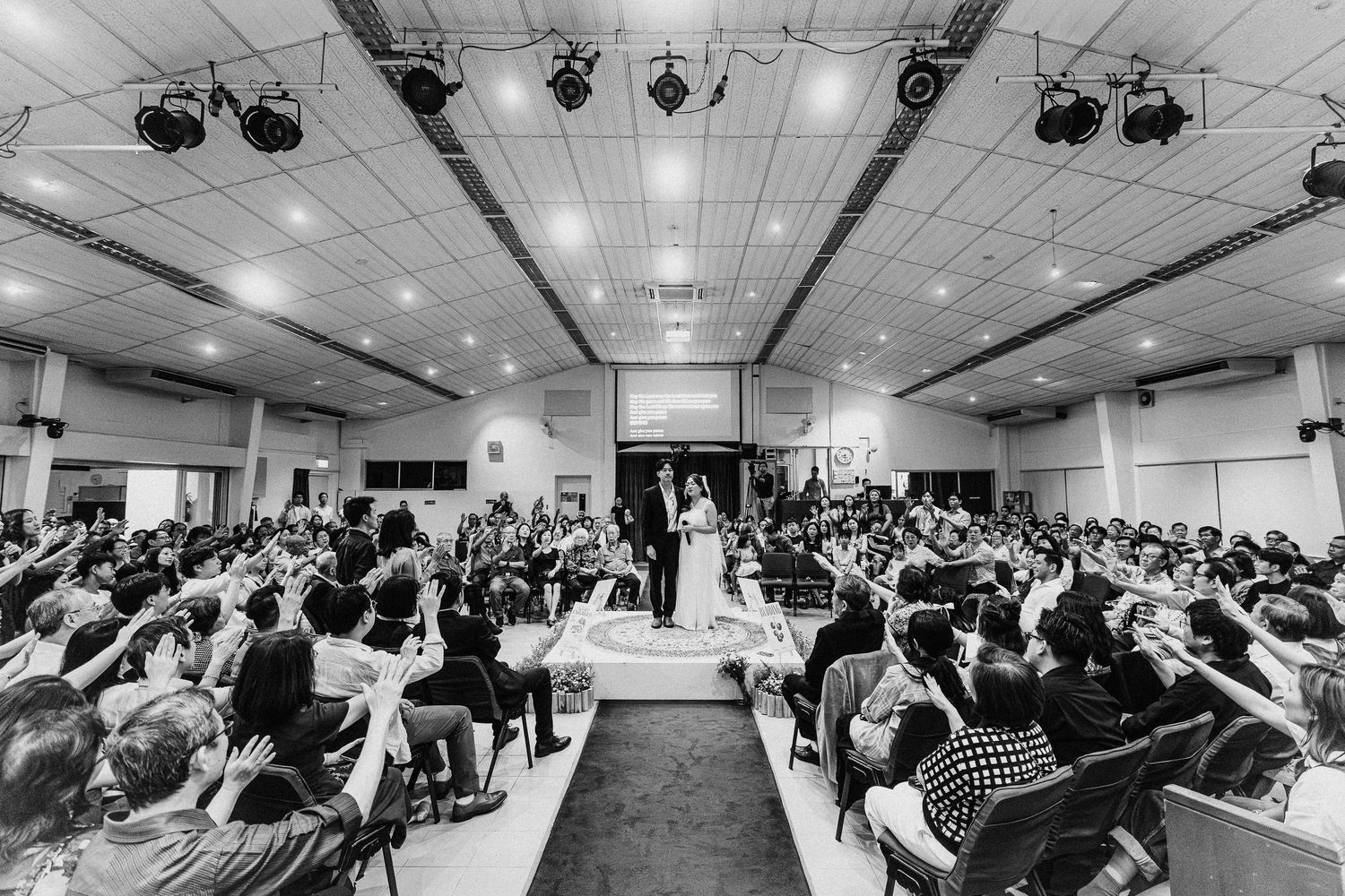 Wide angle black and white shot of wedding ceremony in packed indoor venue.