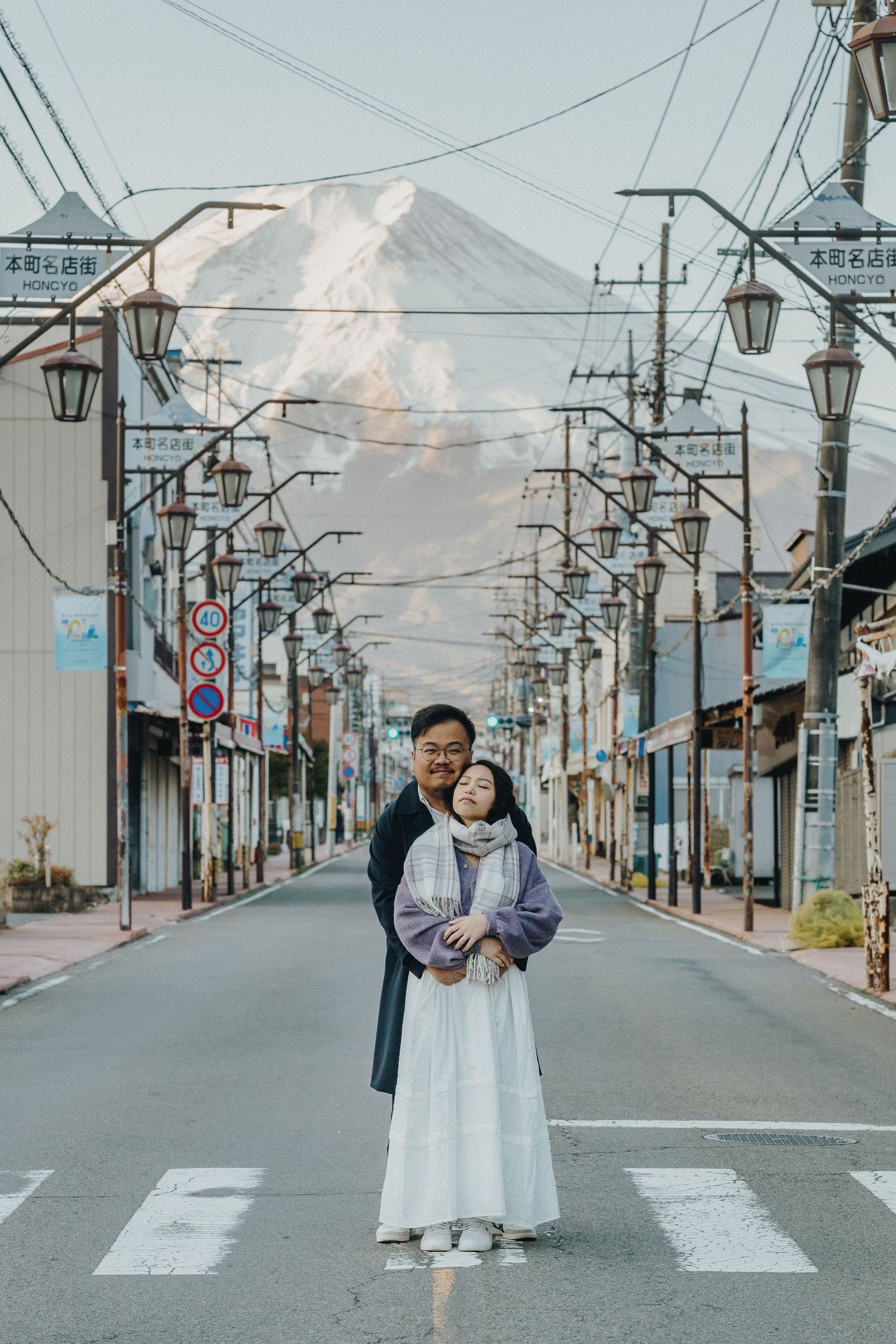 Street scene in Japan with Mount Fuji visible through power lines and traditional lamp posts.
