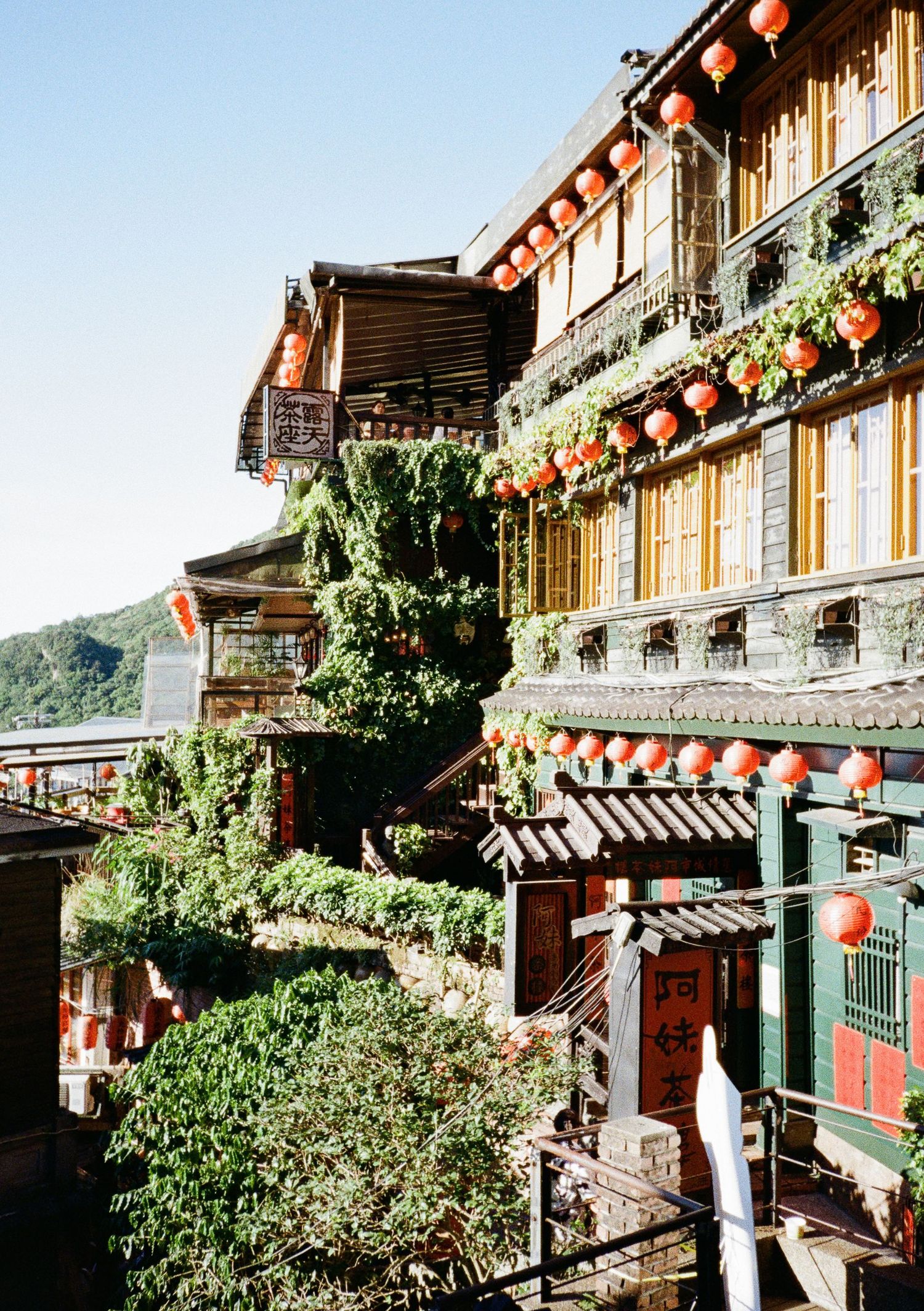 Traditional Chinese architecture with red lanterns hanging from wooden buildings decorated with plants and ornate details.
