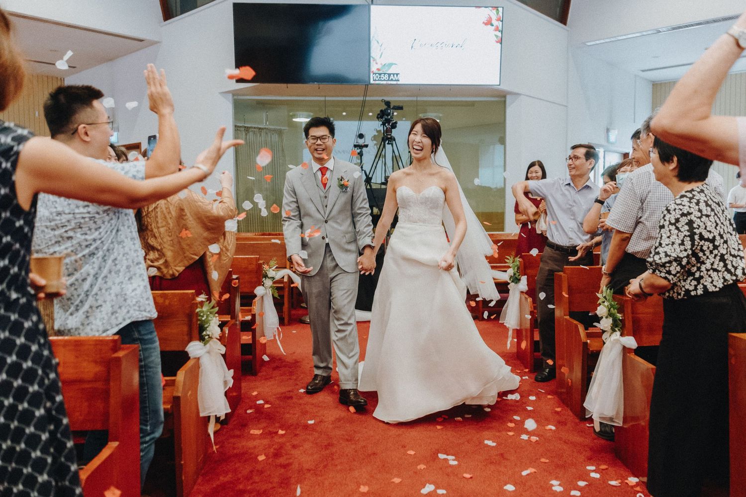Guests shower confetti on the newlyweds walking down the aisle in a church with red carpet.