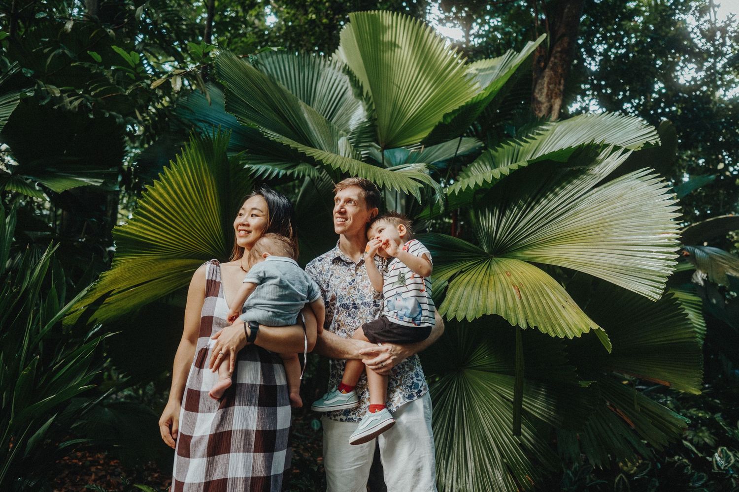 Family standing together against large tropical fan palm leaves in garden setting.